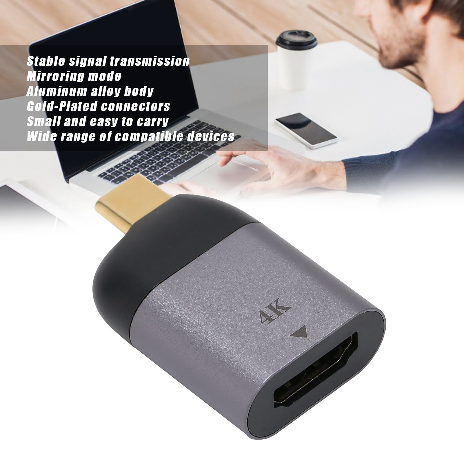 Person hält einen grauen 4K-HDMI-zu-USB-C-Adapter. Ein Laptop im Hintergrund.
