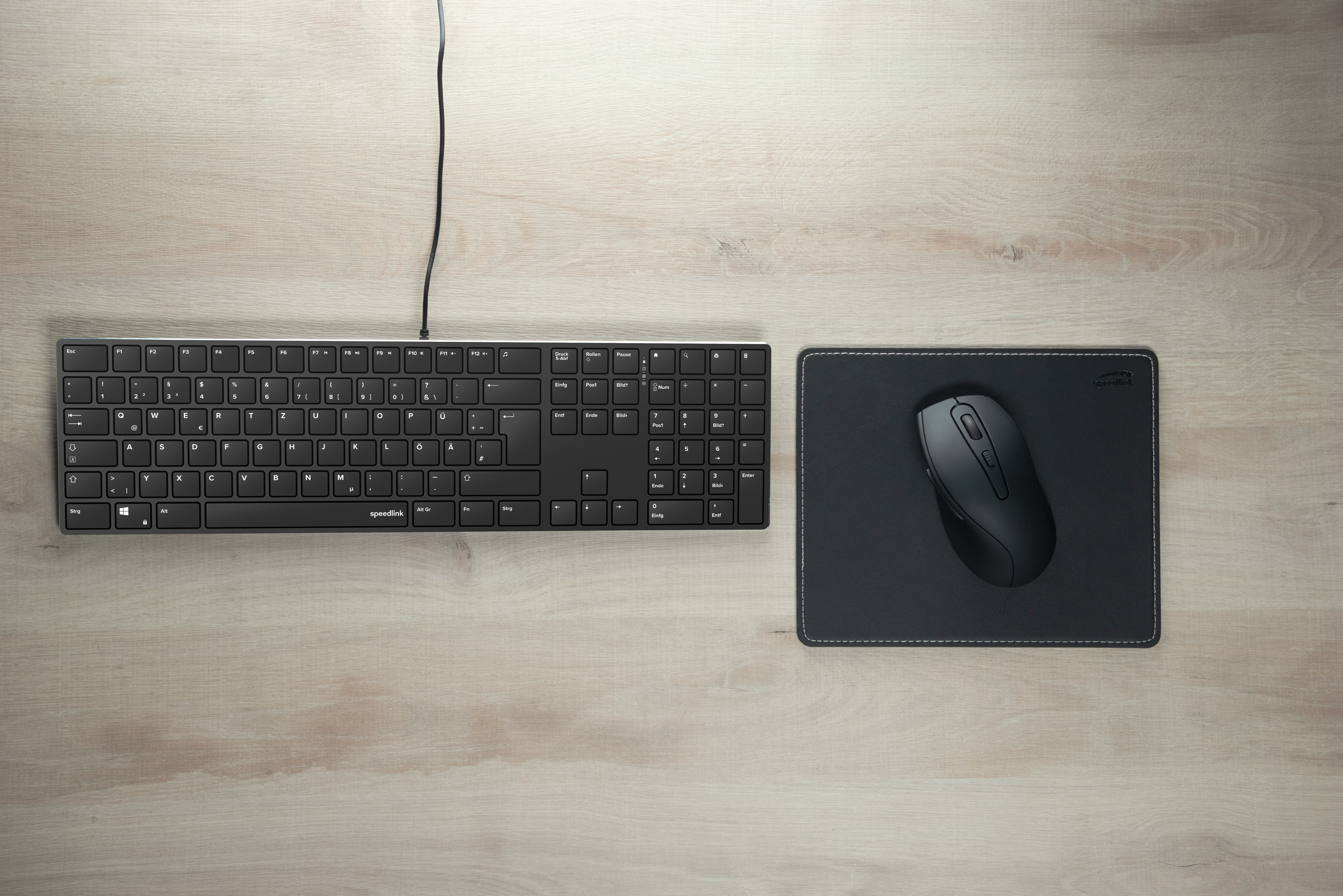 Klawiatura i mysz na drewnianym biurku. Mysz czarna i na czarnej podkładce.