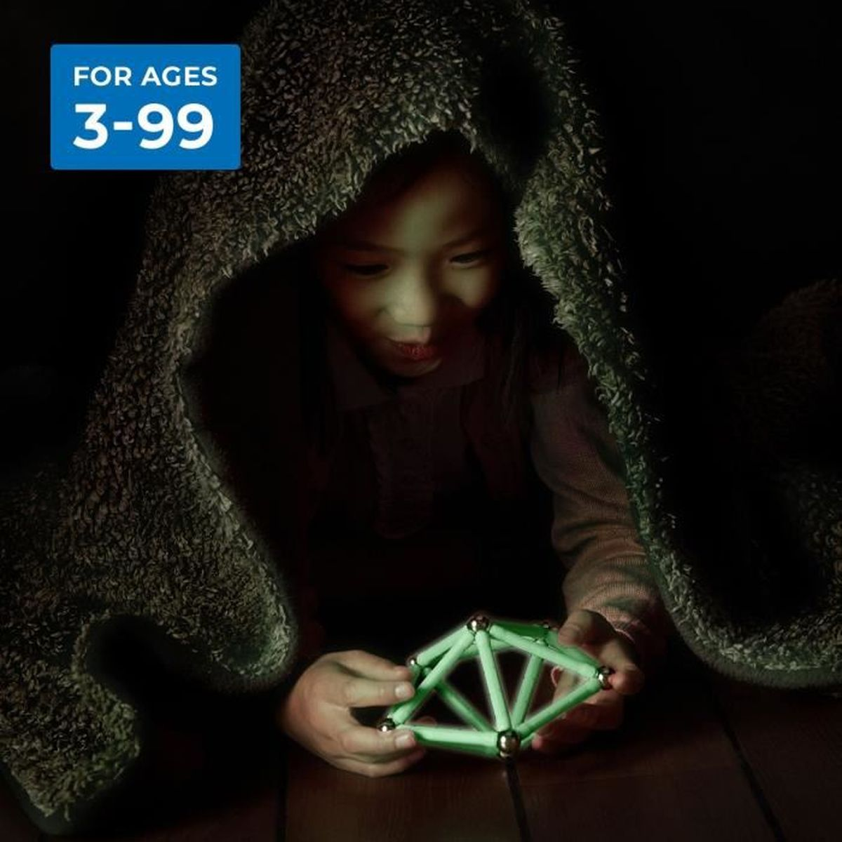 Bambino che guarda un giocattolo verde sotto una coperta. Il giocattolo è nelle sue mani, illuminato.
