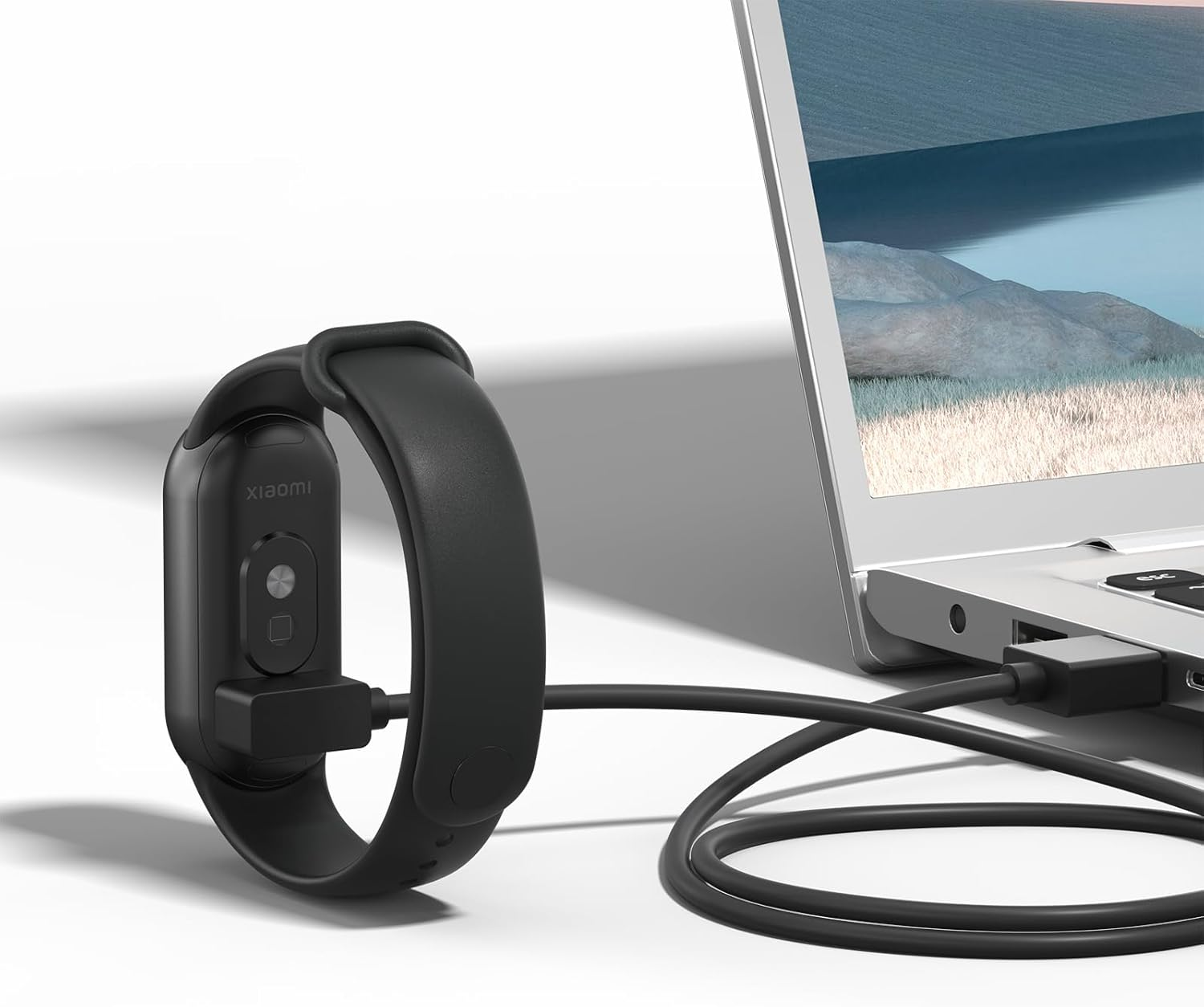 Eine schwarze Smartwatch ist über ein USB-Kabel zum Aufladen mit einem Laptop verbunden.