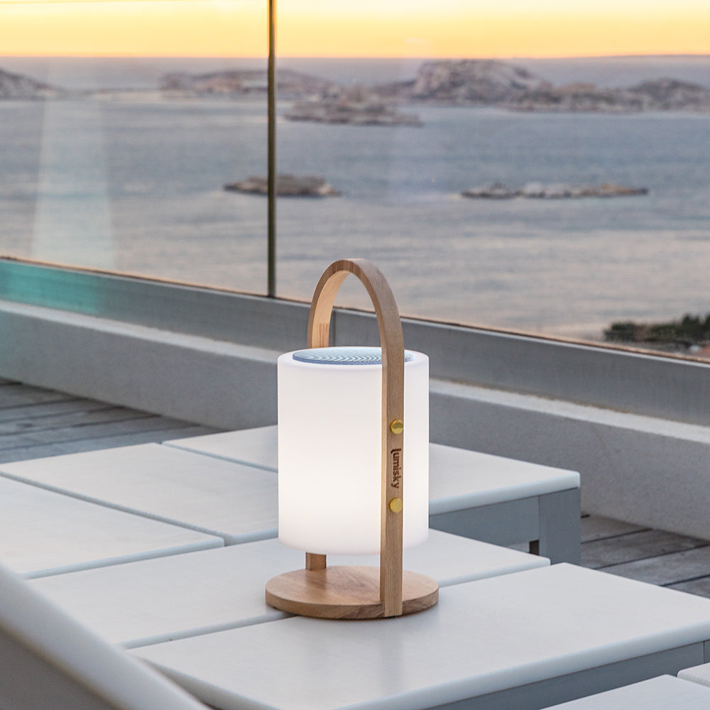 Una moderna lampada bianca e legno su un tavolo bianco, con una vista costiera panoramica sullo sfondo.