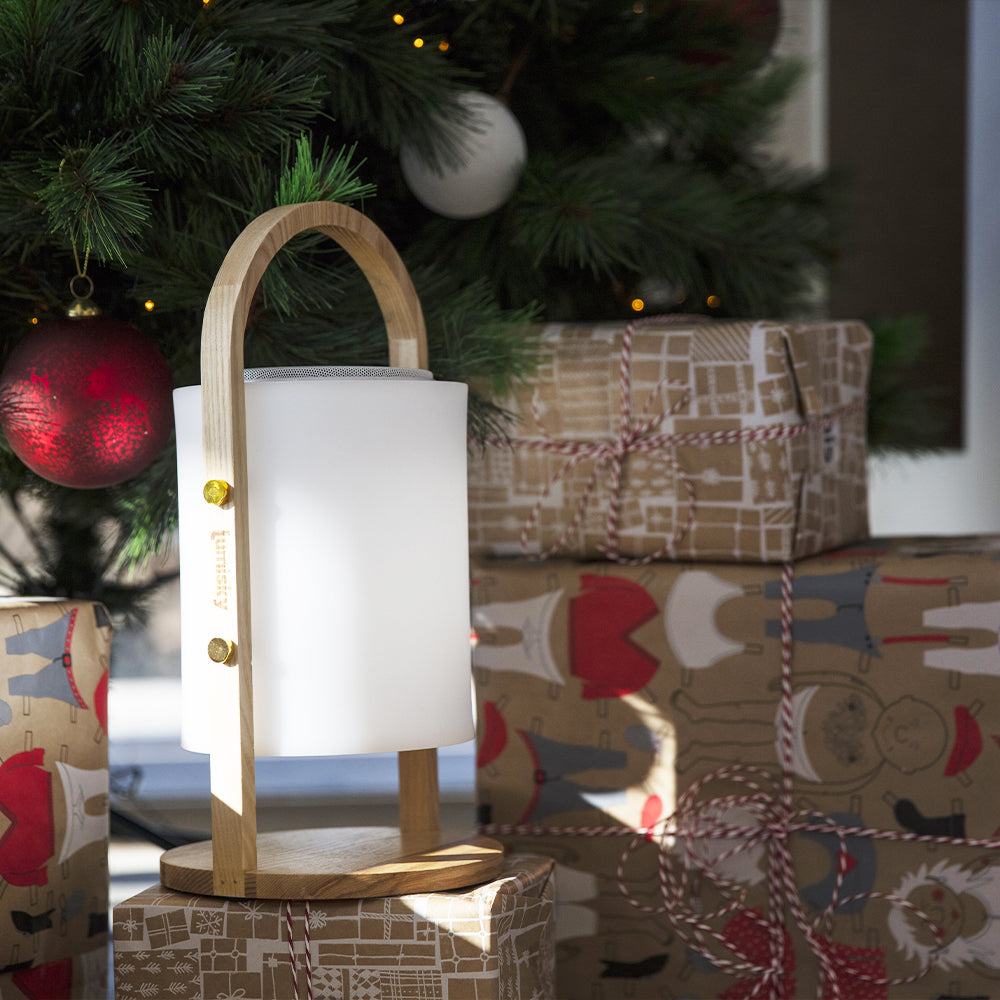 Una lampada Lumisky su scatole regalo sotto un albero di Natale con decorazioni. Regali e albero sullo sfondo.