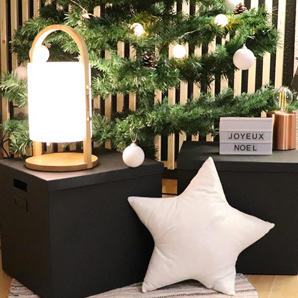 Una lampada Lumisky su una scatola nera con un cuscino a forma di stella e un albero di Natale sullo sfondo.