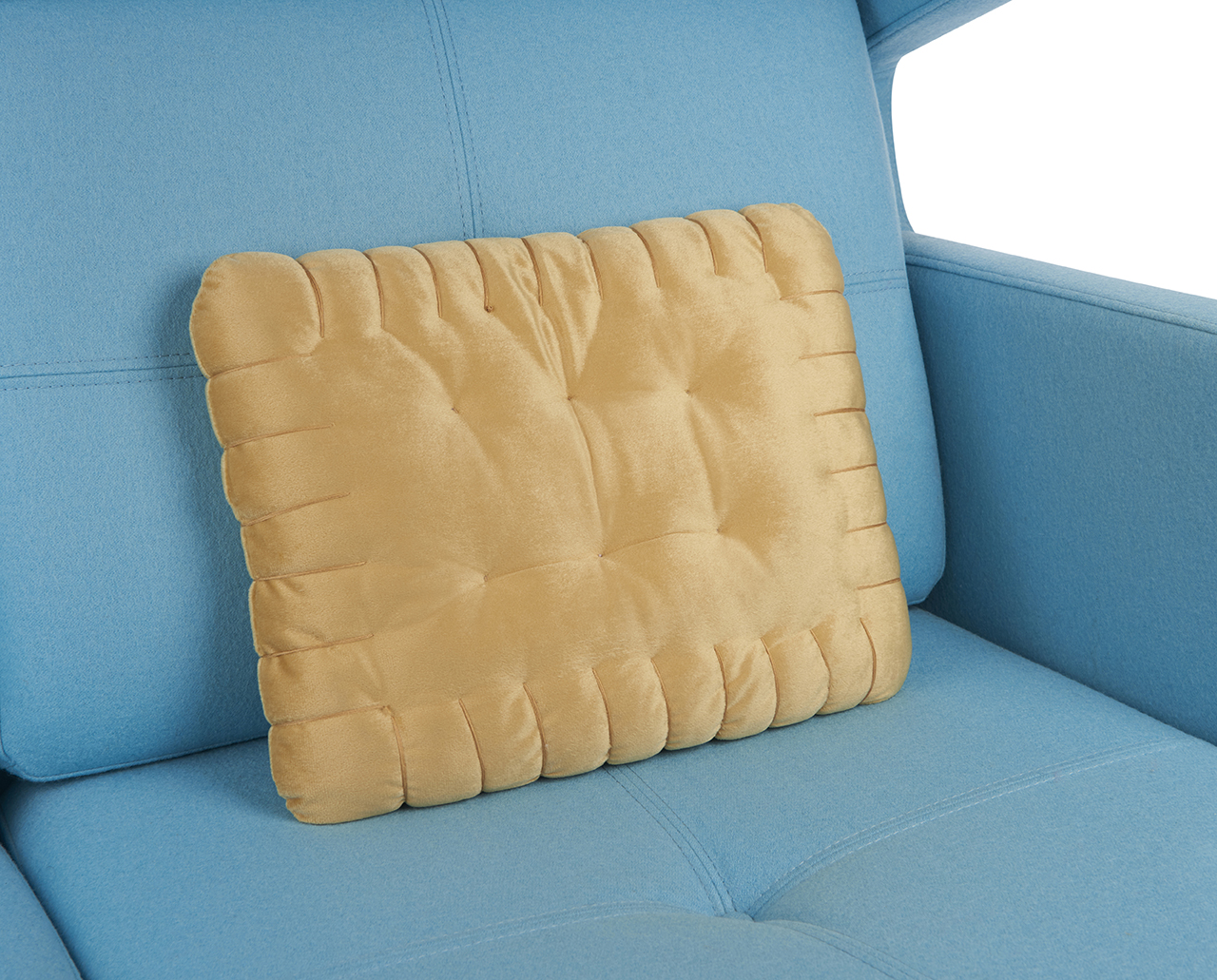 Tanfarbenes rechteckiges Kissen auf einem hellblauen Sofa, geformt wie ein Keks.