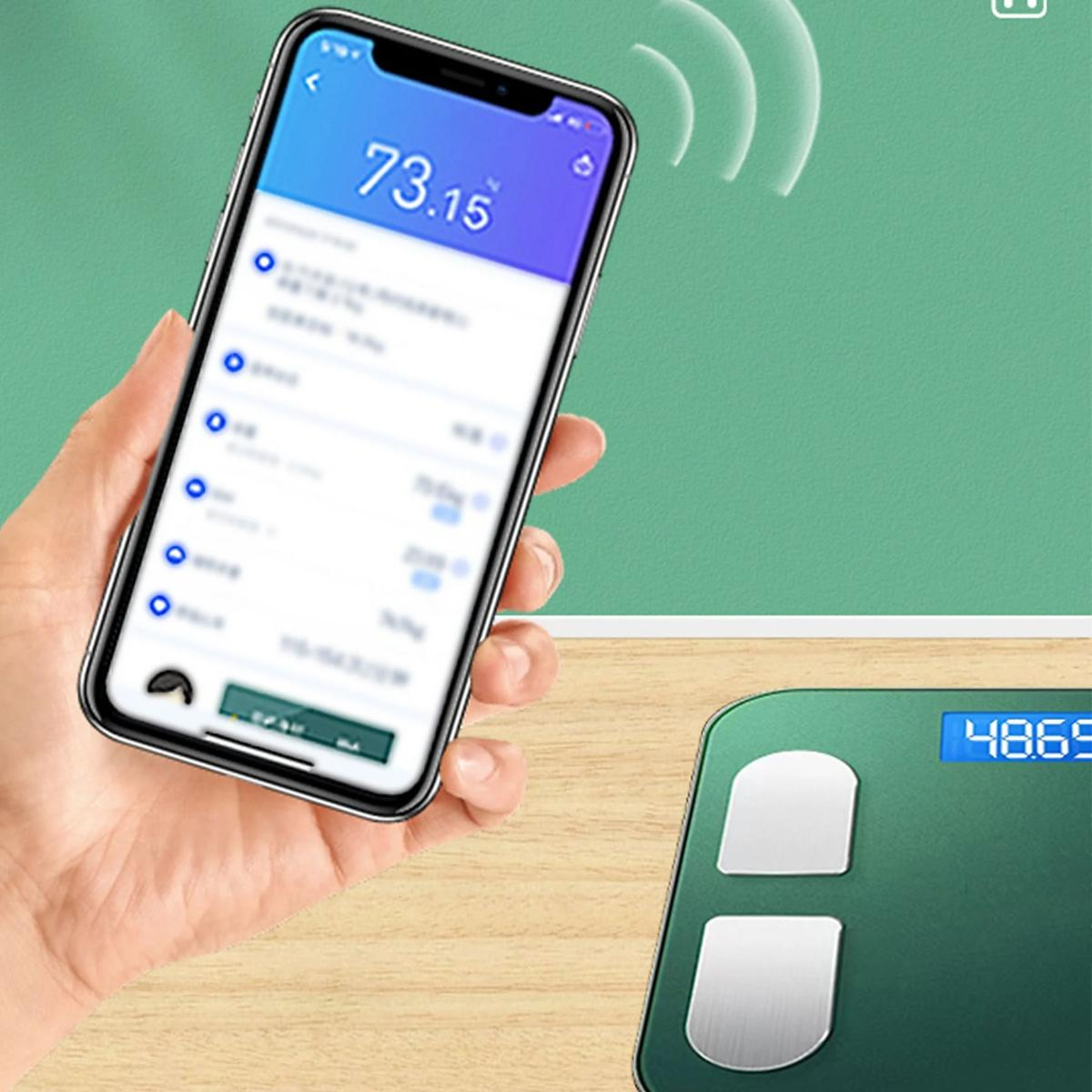 Eine Person hält ein Telefon mit Gewichtsdaten neben einer grünen Waage. Grüner und Holz Hintergrund.