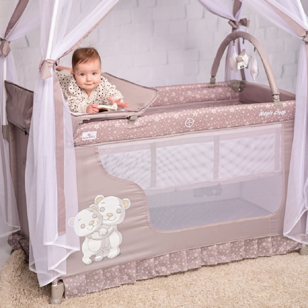 Baby in einem Reisebett, taupefarben mit Sternen, weißem Baldachin und Bären. Heller Hintergrund.