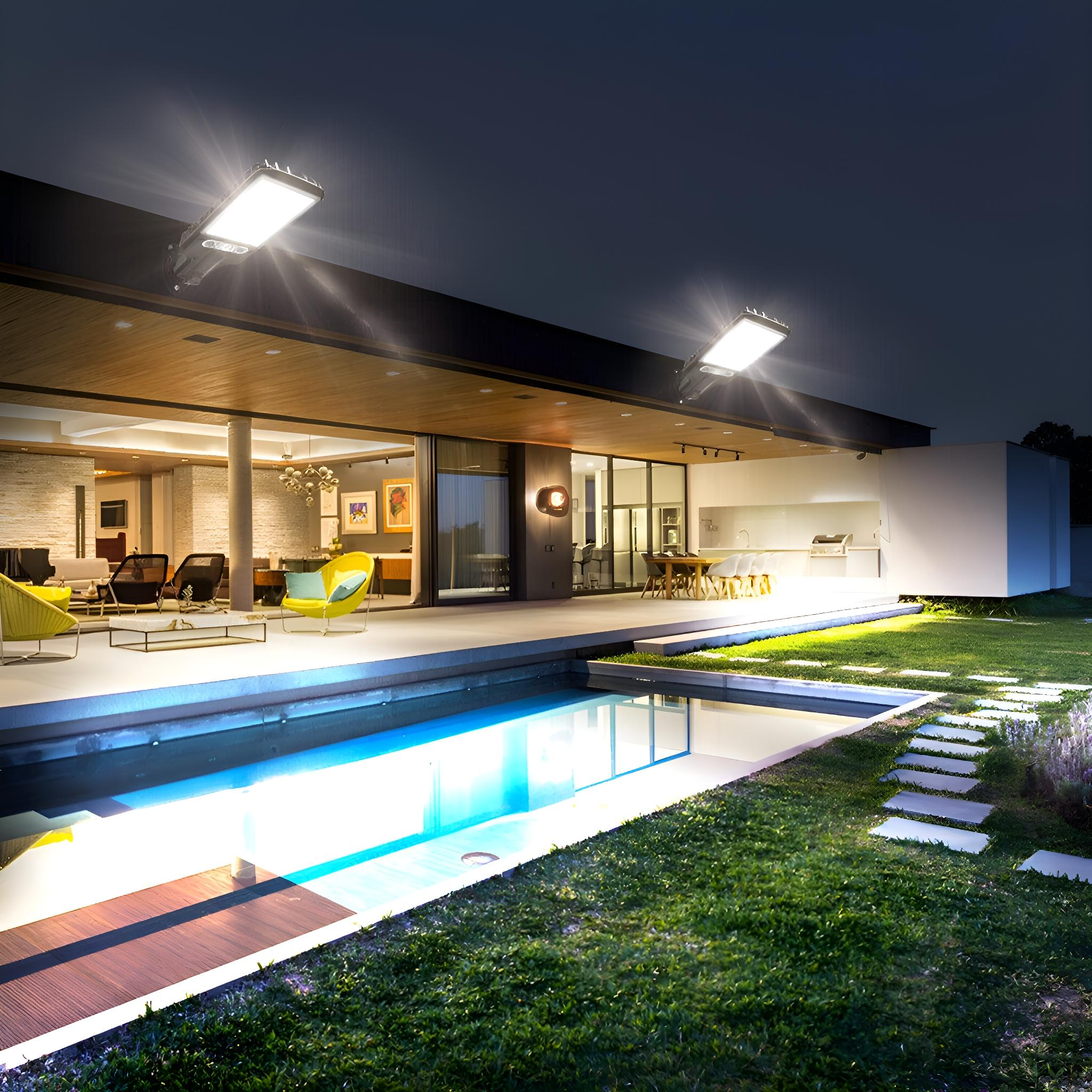 Außenansicht, zwei Lichter über einem Pool bei Nacht. Im Hintergrund ein Haus mit beleuchtetem Innenraum.