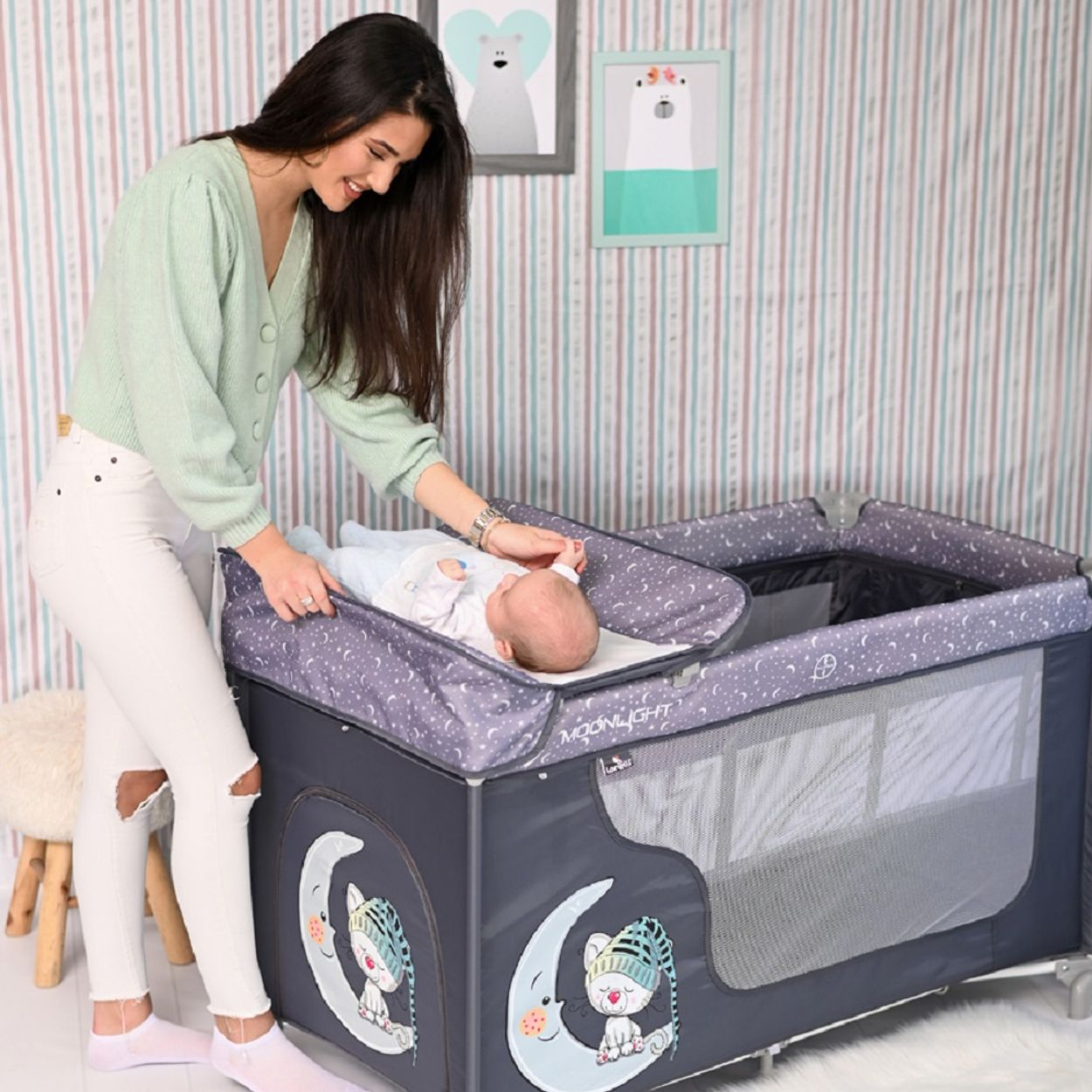 Frau beugt sich über ein Baby in einem Kinderbett. Im Hintergrund sind Zeichnungen von Bären.