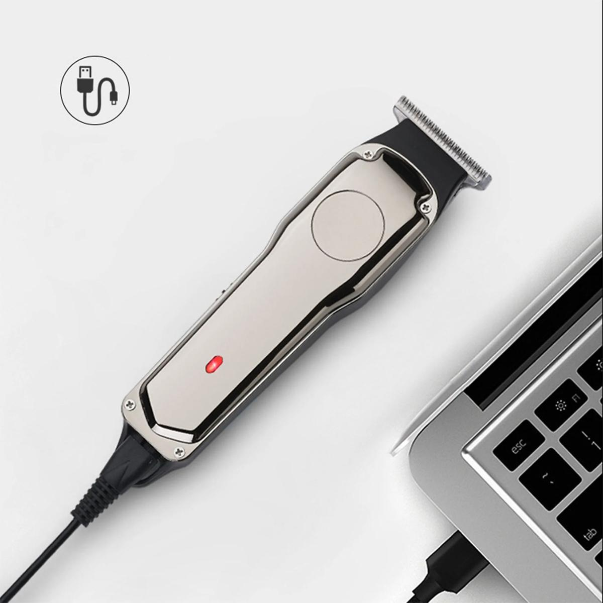 Ein silberner Haarschneider, der über ein Ladekabel an einen Laptop angeschlossen ist, mit roter Ladeanzeige.