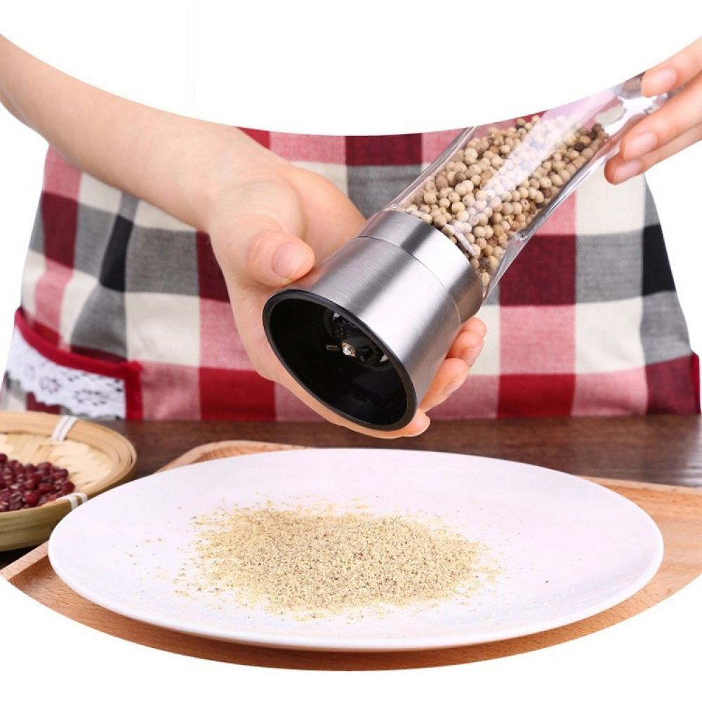 Eine Person, die Pfefferkörner mit einer Mühle auf einen weißen Teller mahlt, mit einer Schüssel mit roten Bohnen und einem Holzbrett.