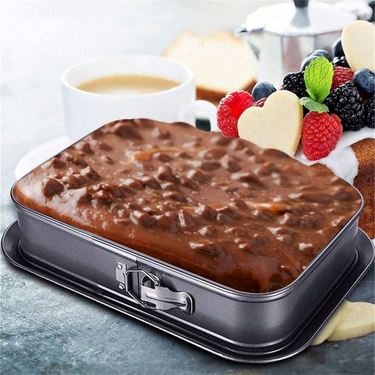 Ein rechteckiger Kuchen in einer Backform mit Schokoladenbelag, umgeben von Früchten.