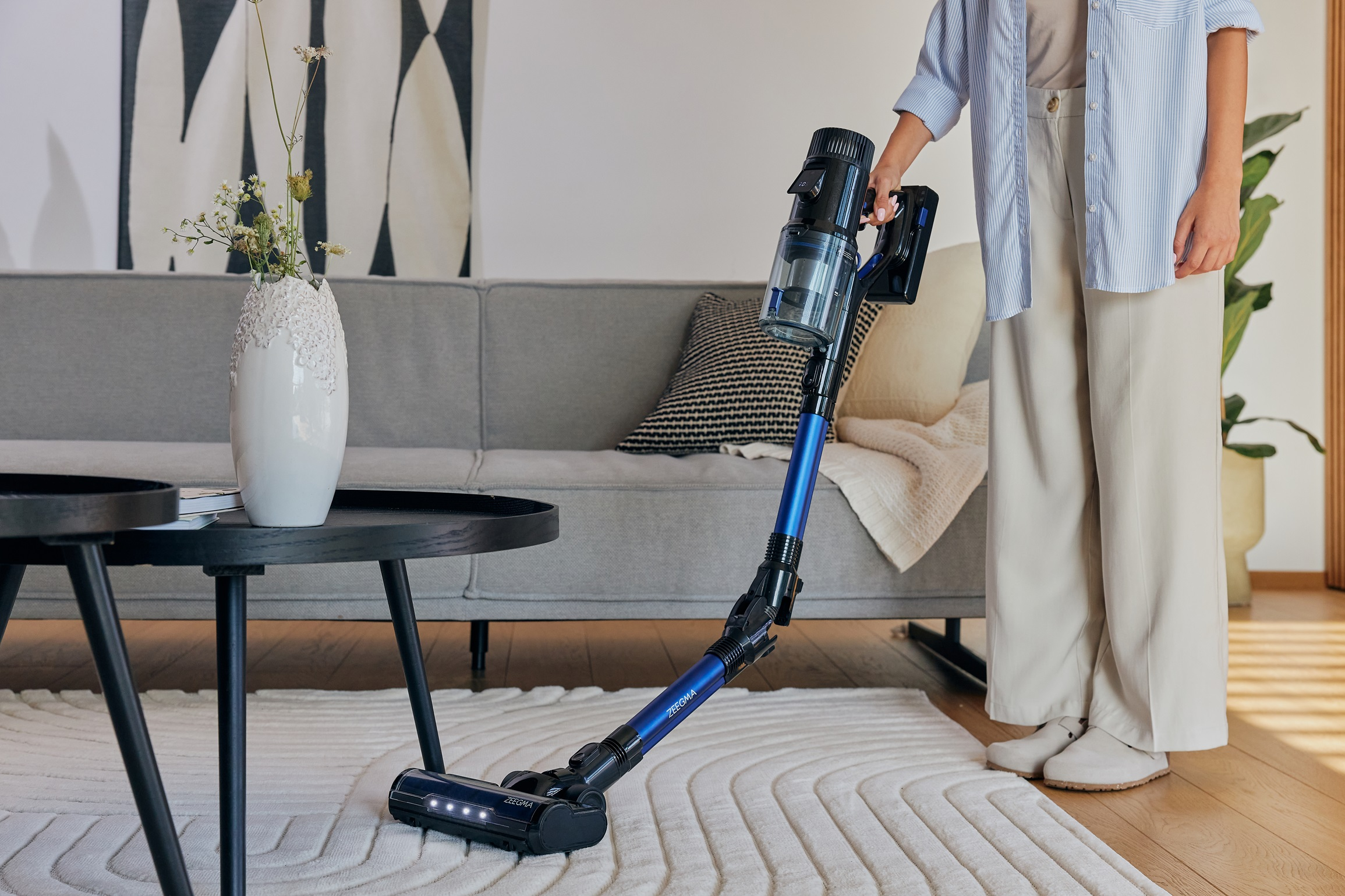 Kobieta odkurza dywan odkurzaczem bezprzewodowym w nowoczesnym salonie.