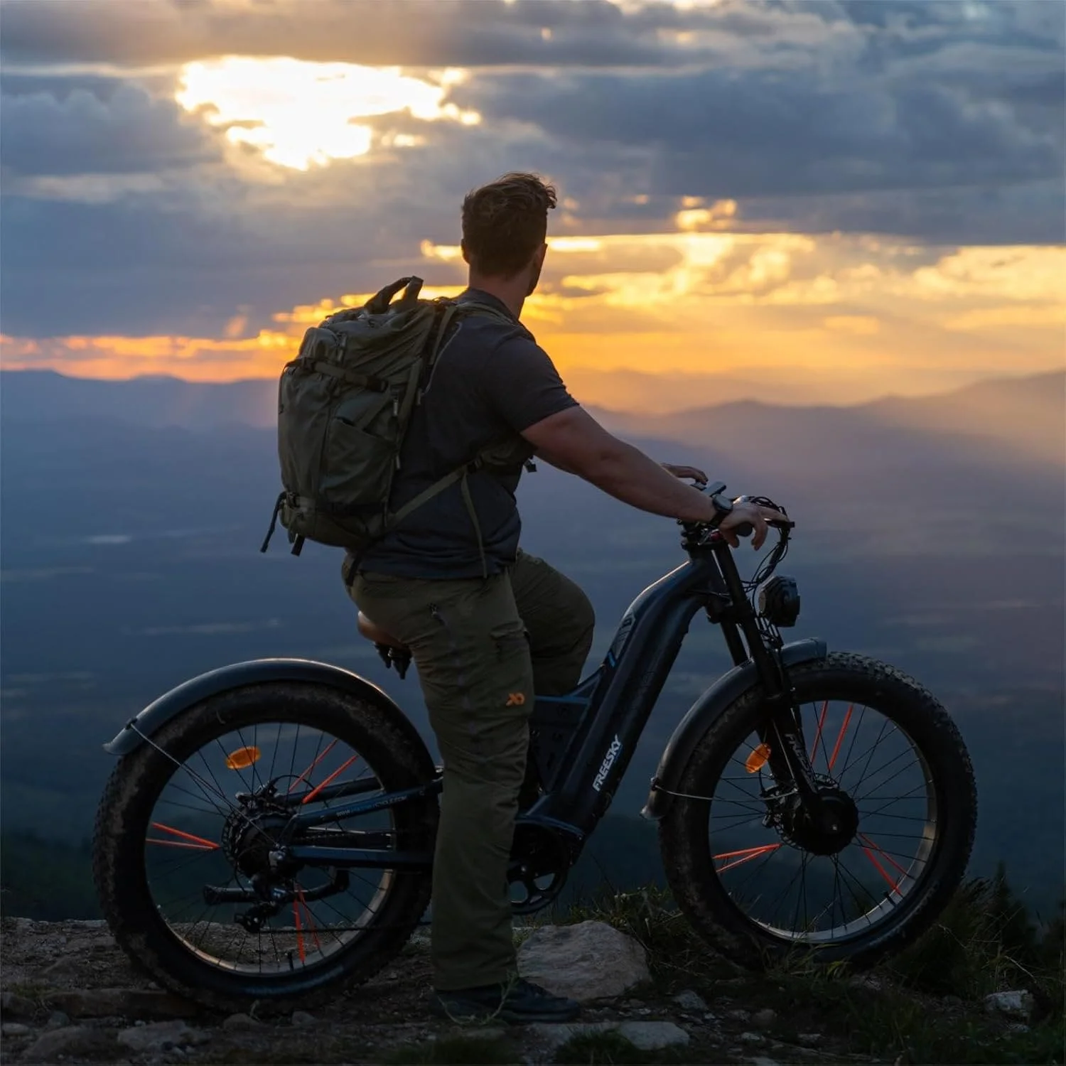 Mann auf einem Fatbike, bei Sonnenuntergang, mit Blick auf ein Gebirge.
