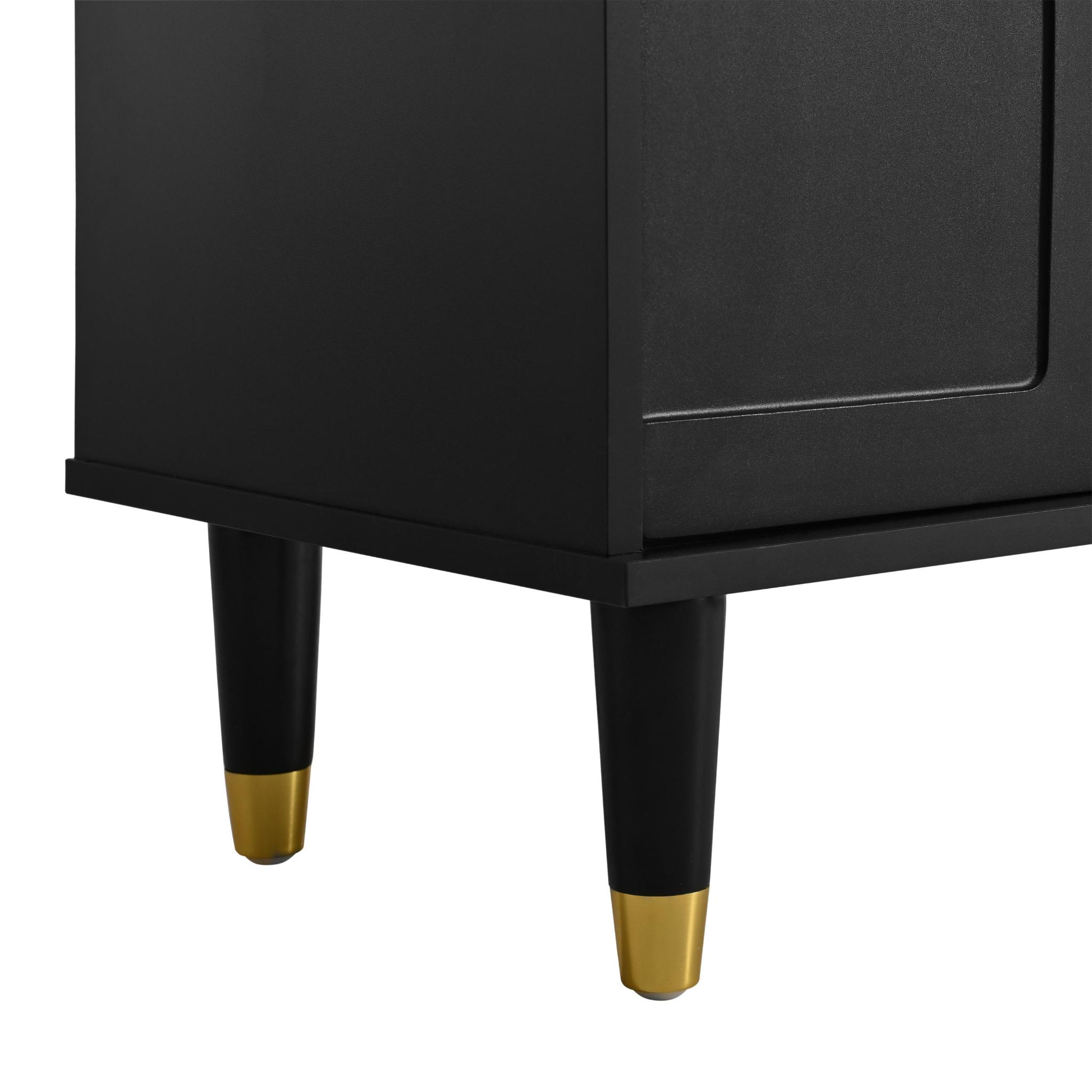 Detail eines schwarzen Schranks. Der Schrank hat schwarze Beine mit goldenen Kappen auf weißem Hintergrund.