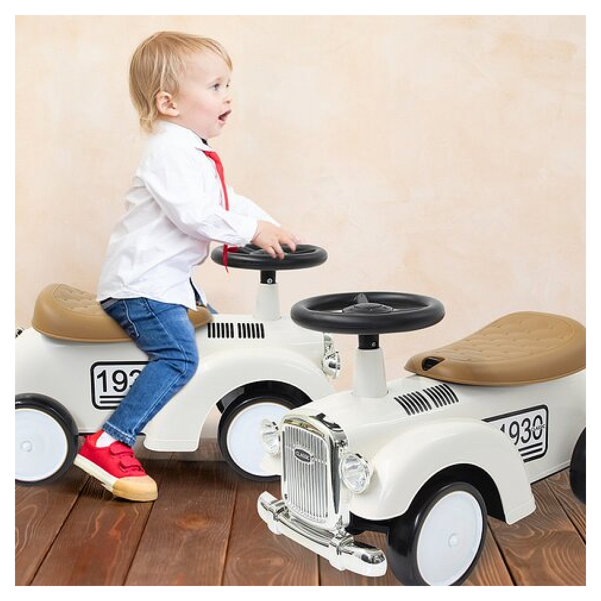 Dziecko w białej koszuli i dżinsach w białym samochodzie zabawce, czerwone buty, drewniana podłoga.
