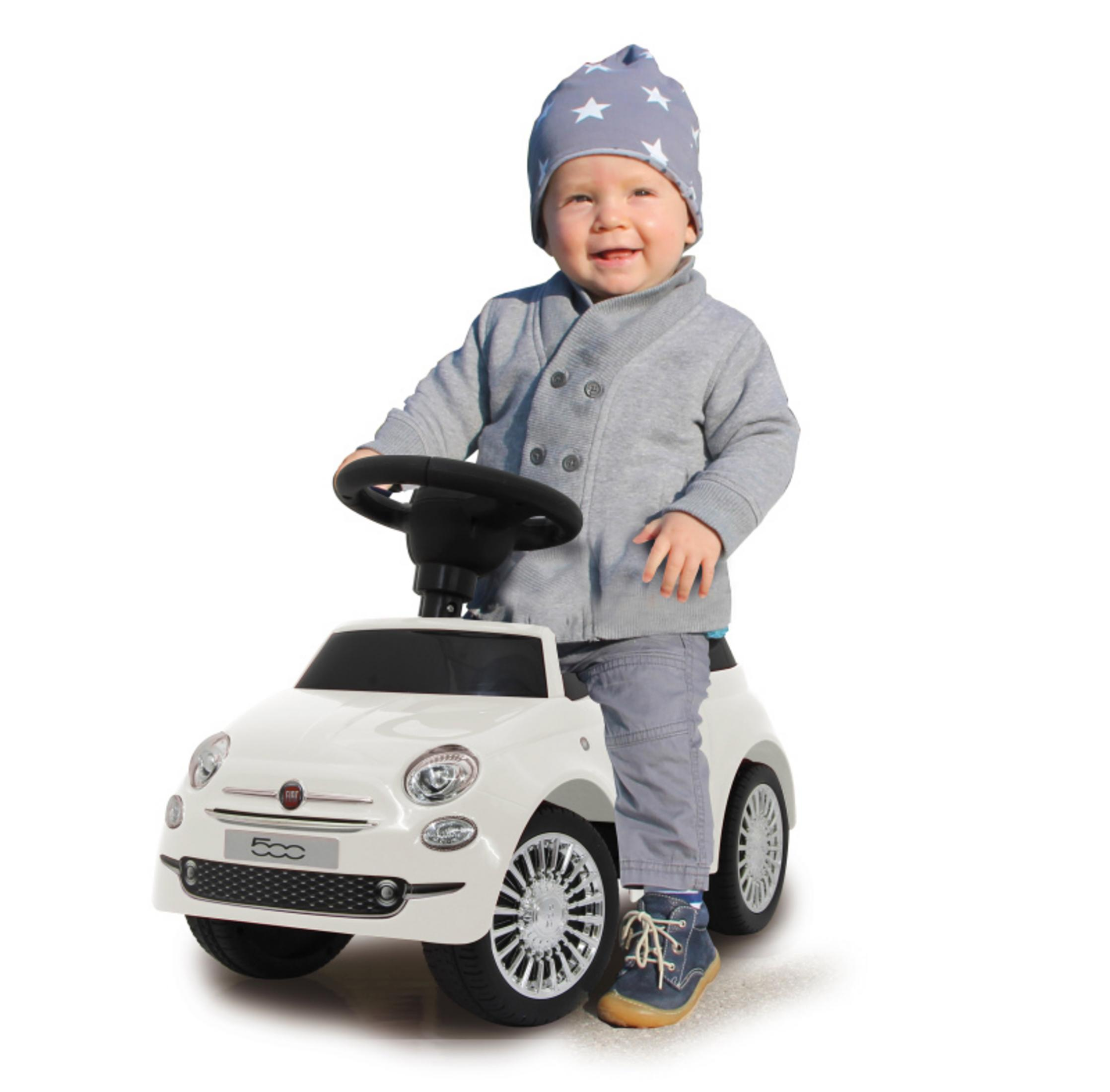 Ein Baby sitzt in einem weißen Spielzeugauto. Das Baby trägt eine blaue Jacke und einen Hut. Das Auto hat ein Fiat-Logo.