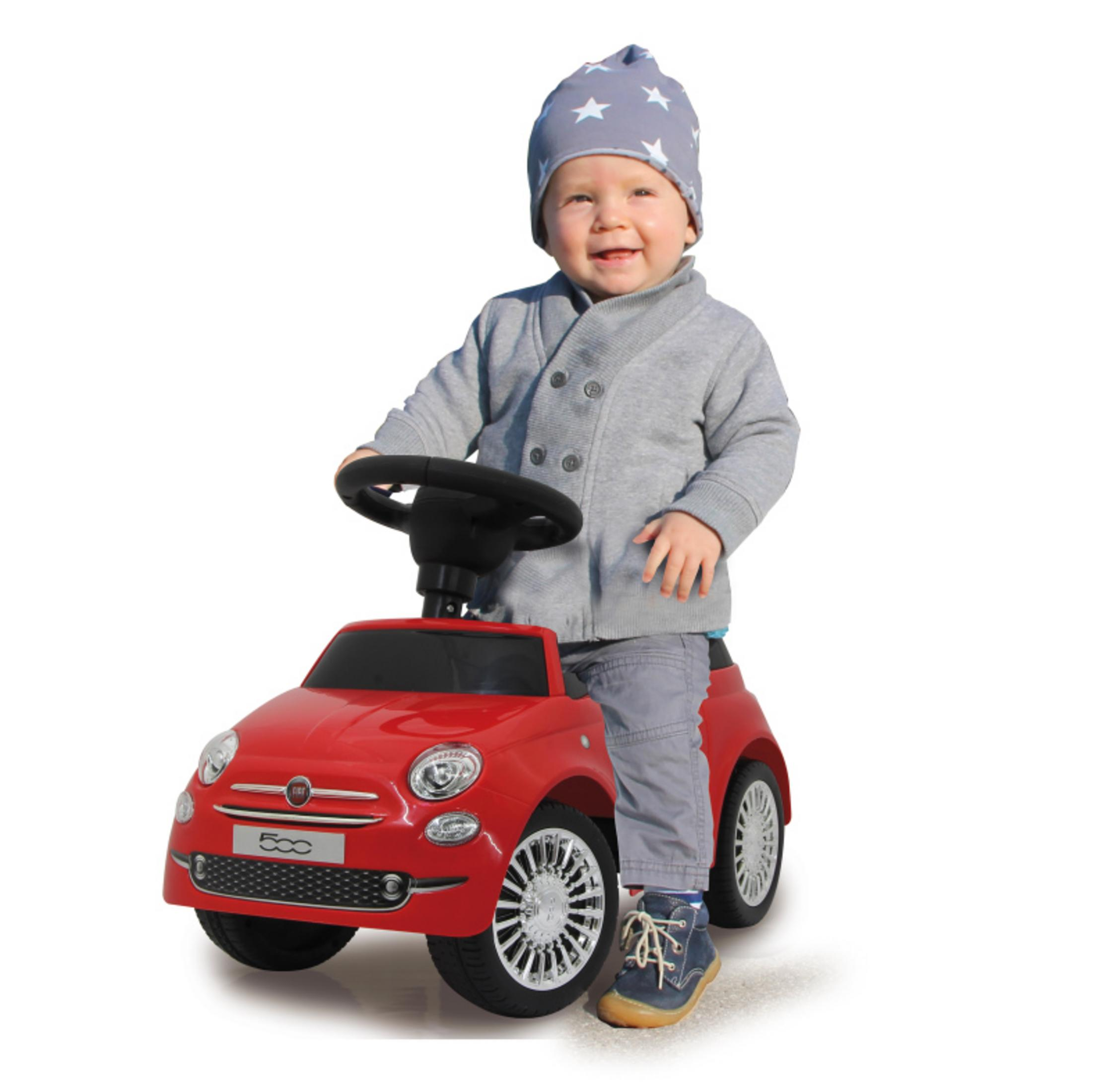 Dziecko oparte o czerwony samochód zabawkowy Fiat 500. Dziecko w czapce i szarej kurtce. Białe tło.