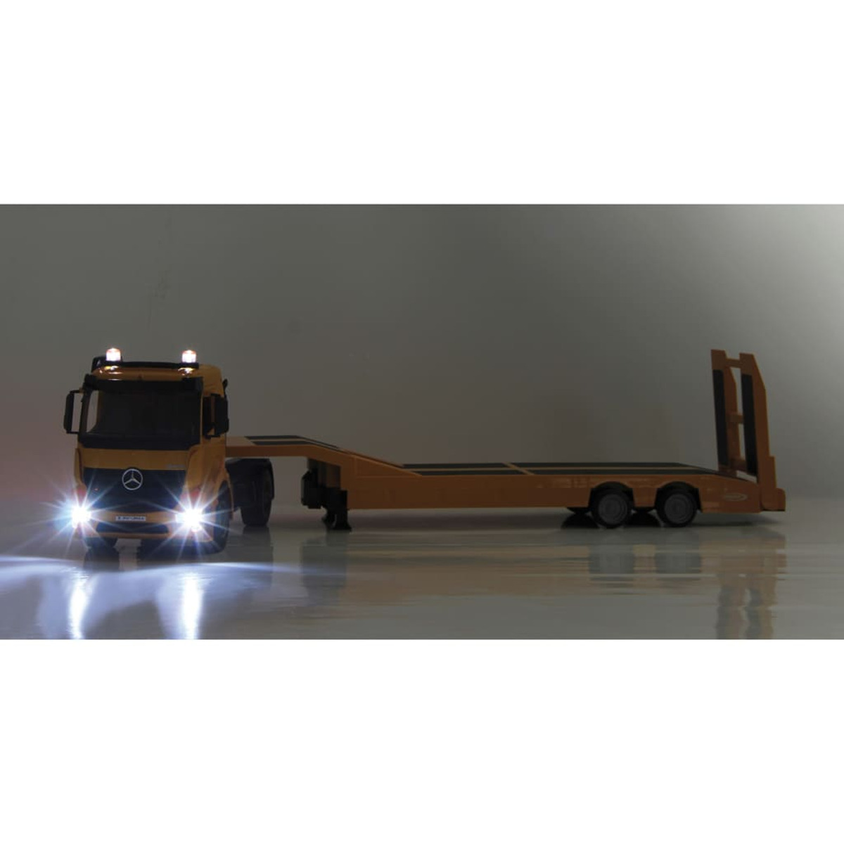 Ein Spielzeug-LKW mit eingeschalteten Scheinwerfern und Rücklichtern, mit Anhänger, auf hellem Hintergrund.