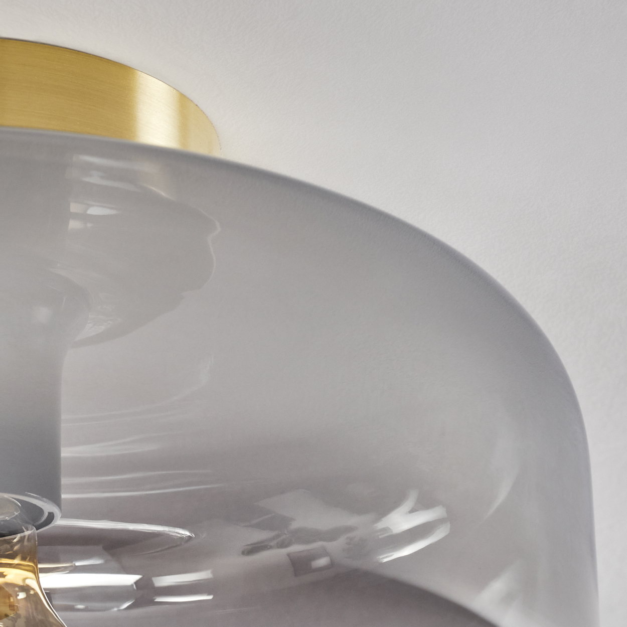 Eine Deckenlampe mit grauem Glasschirm und goldenem Sockel. Im Inneren ist eine Glühbirne sichtbar.