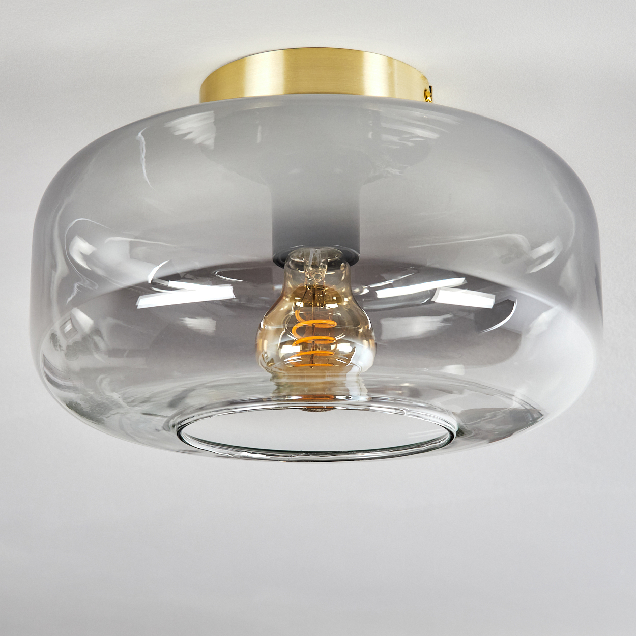 Deckenleuchte mit transparentem Glasschirm und goldenem Sockel, mit sichtbarer Glühbirne im Inneren.
