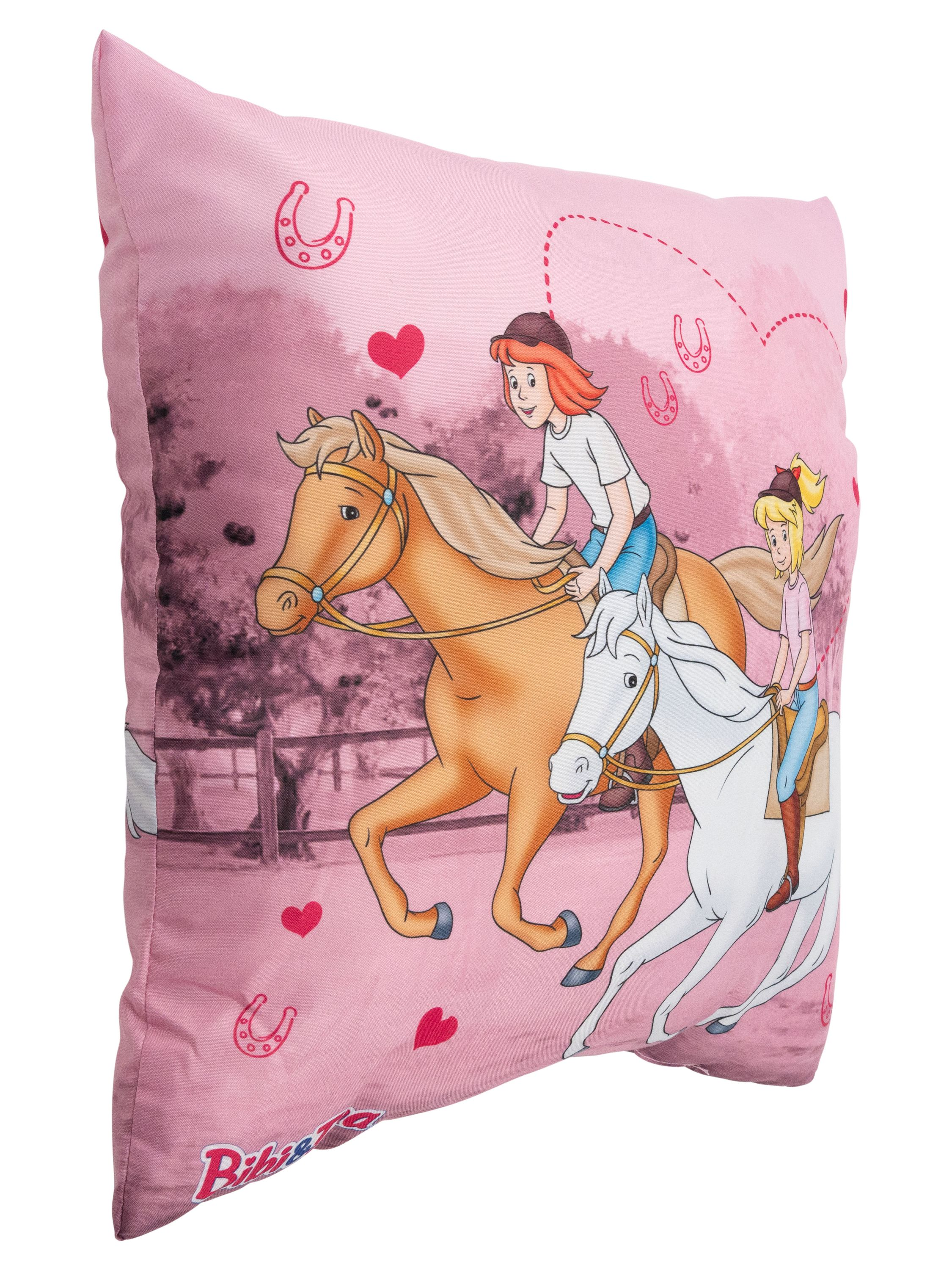 Ein rosa Kissen mit einer Cartoon-Szene von Mädchen, die Pferde auf einem Feld reiten, mit Herzen.