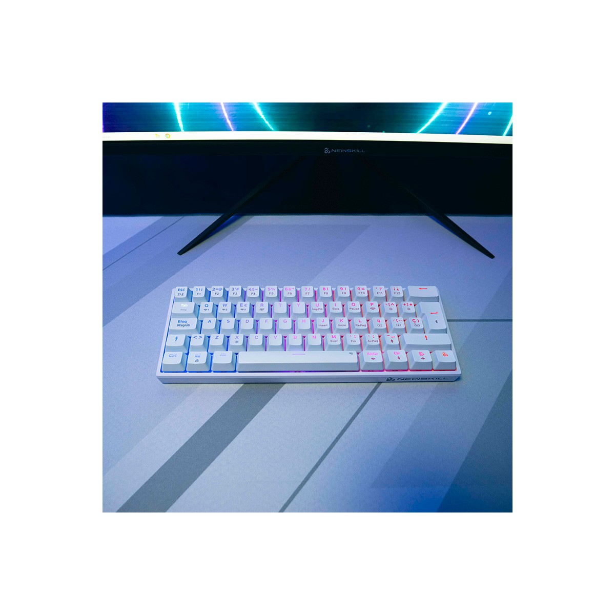 Teclado blanco con teclas coloridas sobre una superficie gris claro. Un monitor está en el fondo. Logotipo de Newskill presente.