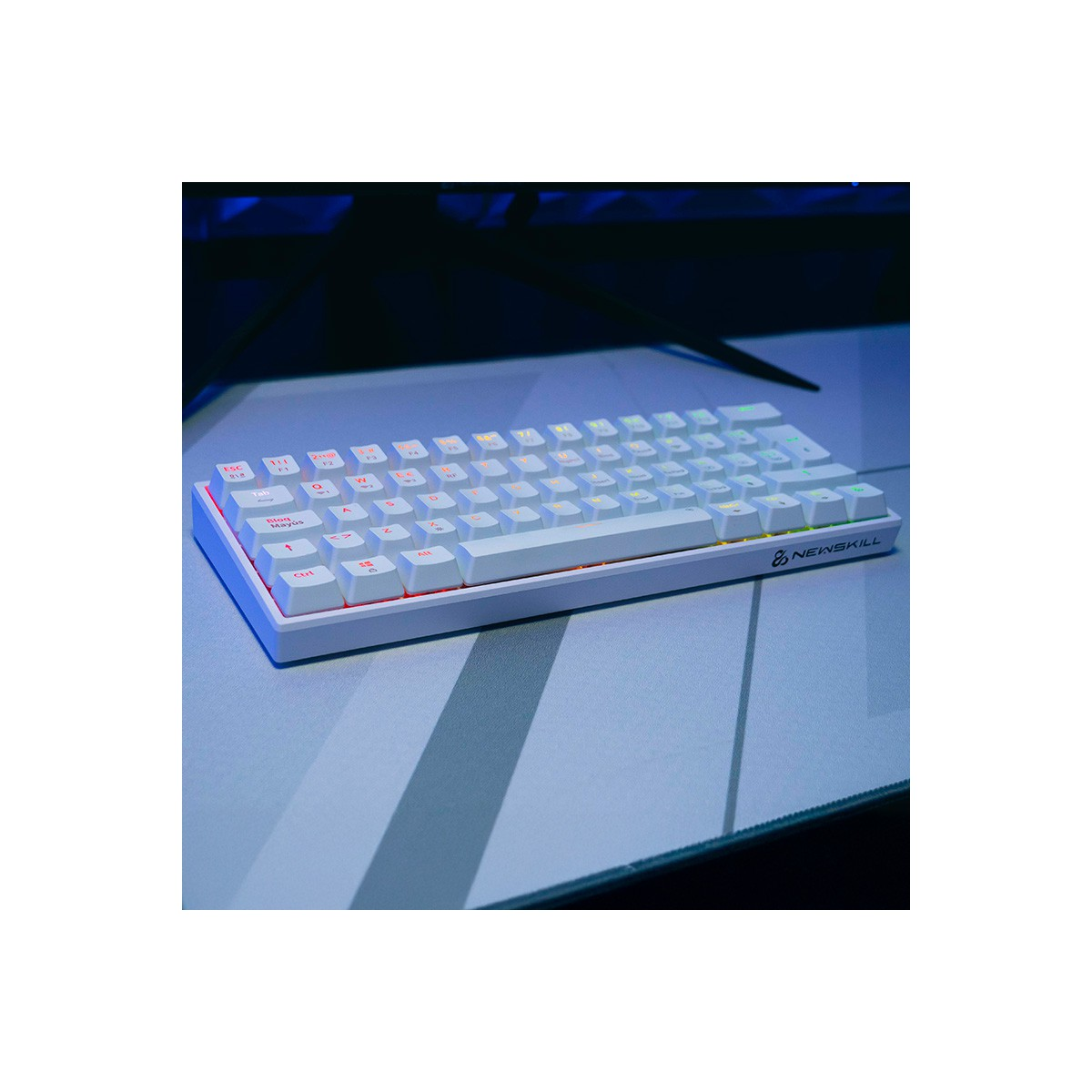 Teclado blanco con teclas coloridas. Un monitor es visible en el fondo. Logotipo de Newskill presente en el teclado.