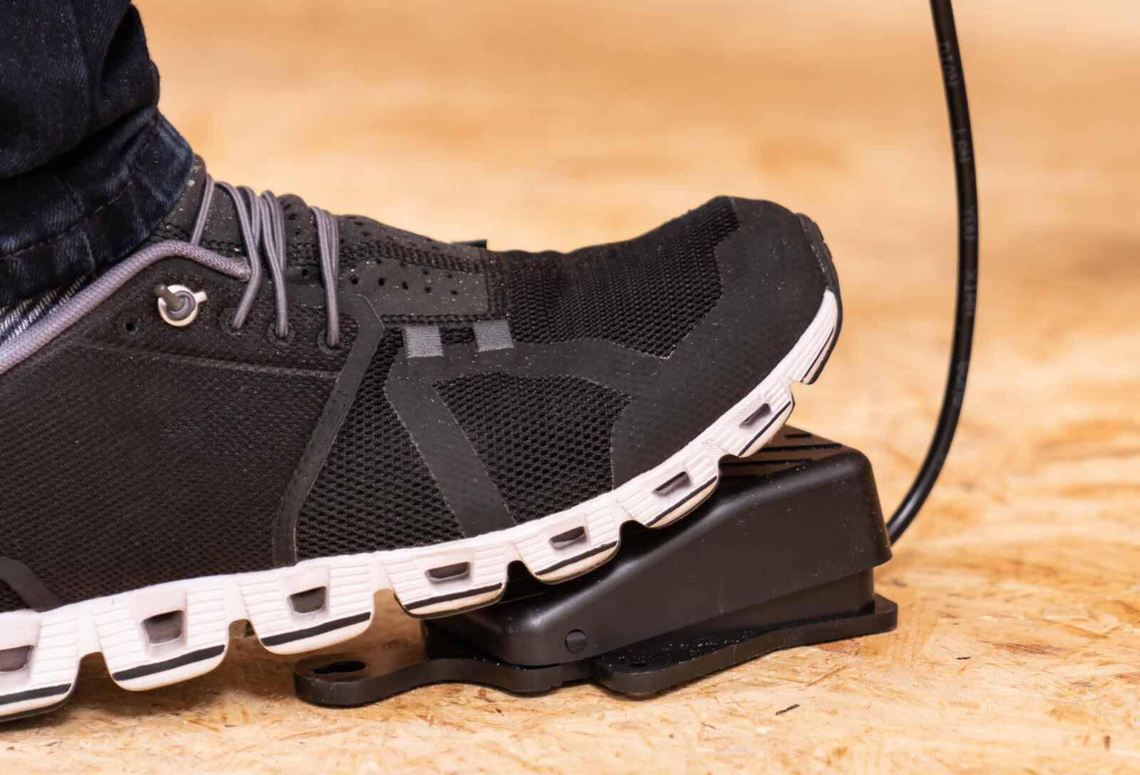 Een zwarte sneaker op een zwart pedaal. De schoen staat op een houten oppervlak.