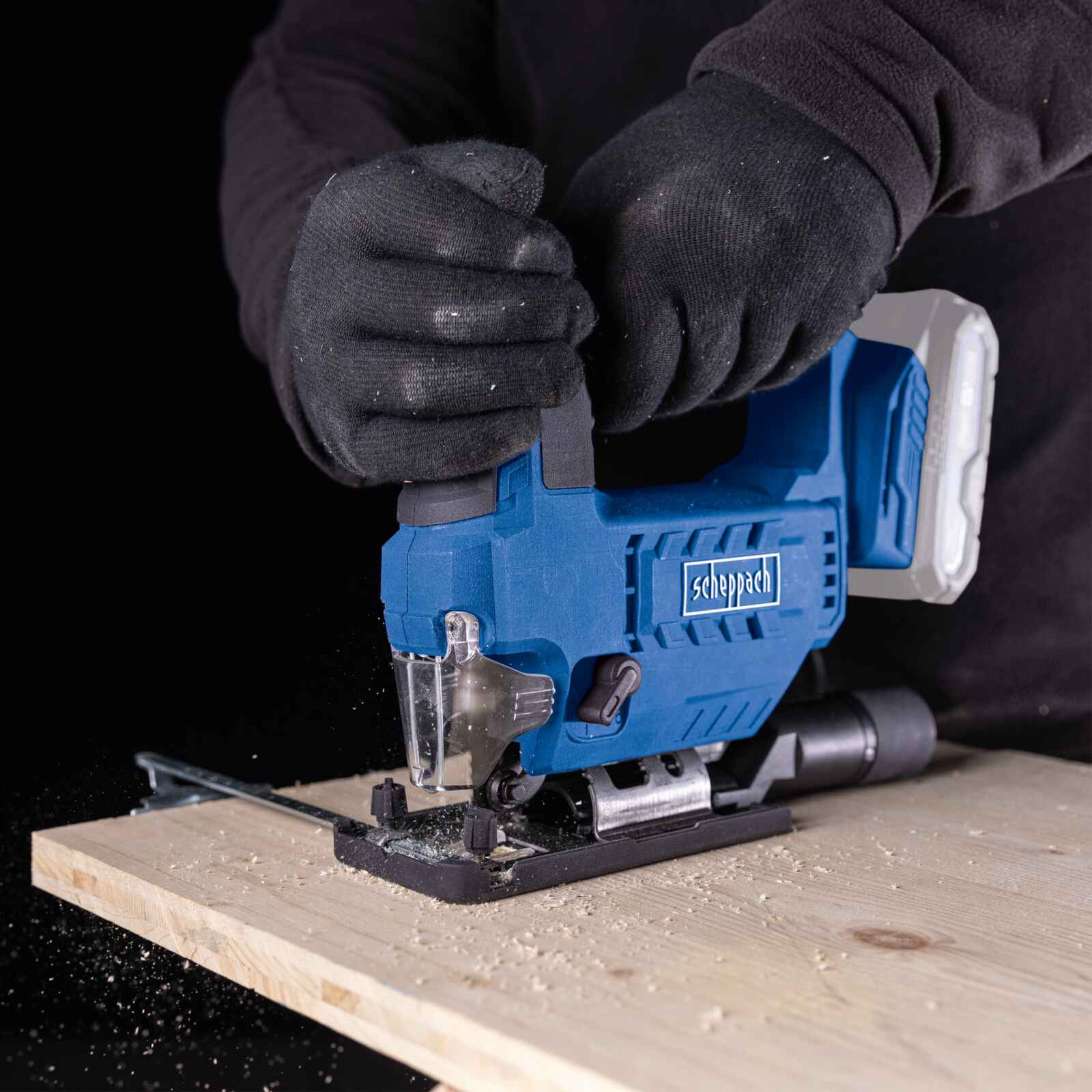 Een persoon gebruikt een blauwzwarte decoupeerzaag op een stuk hout. Zwarte handschoenen worden gedragen.