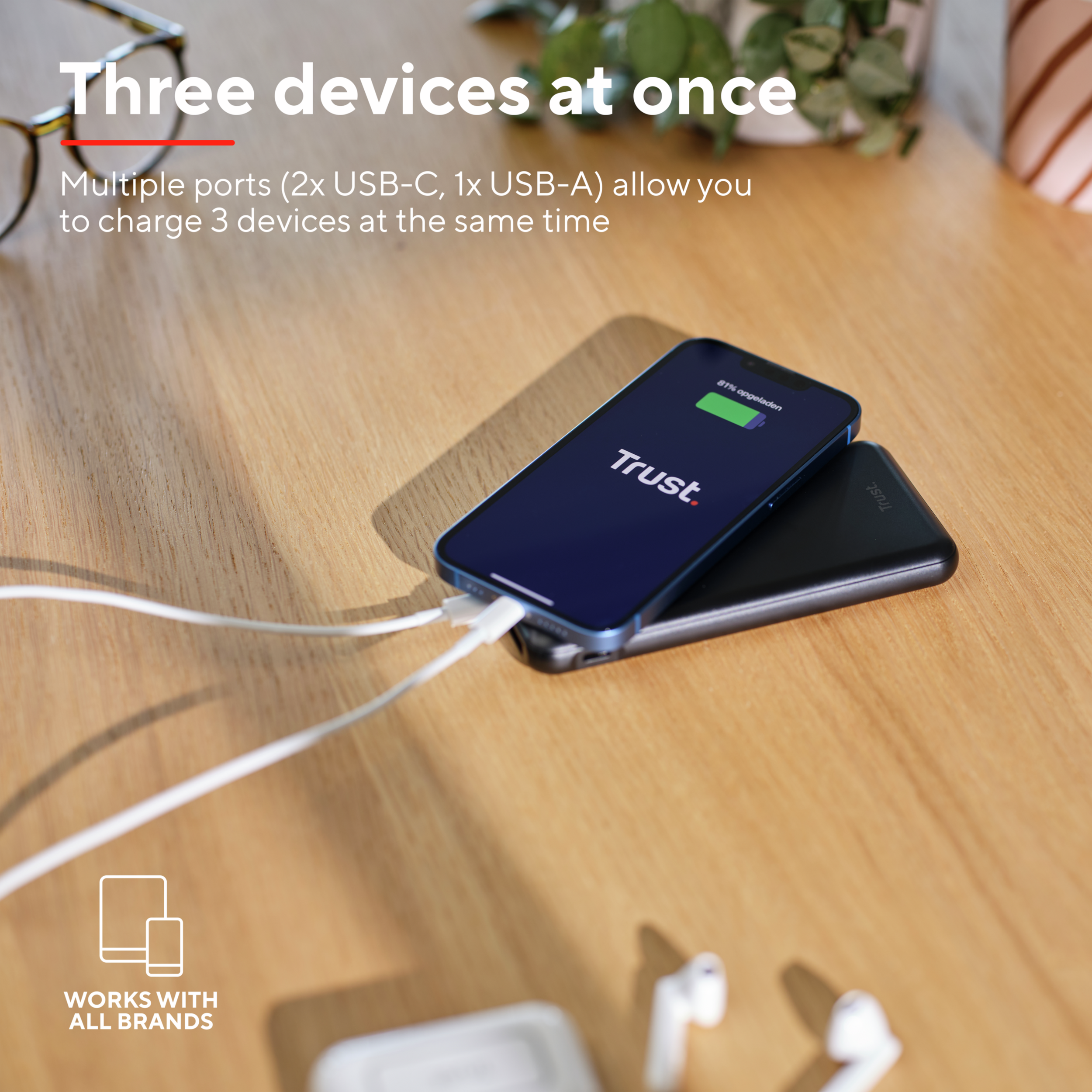 Een telefoon die oplaadt op een zwarte powerbank, een witte kabel en een smartphone met Trust-logo.