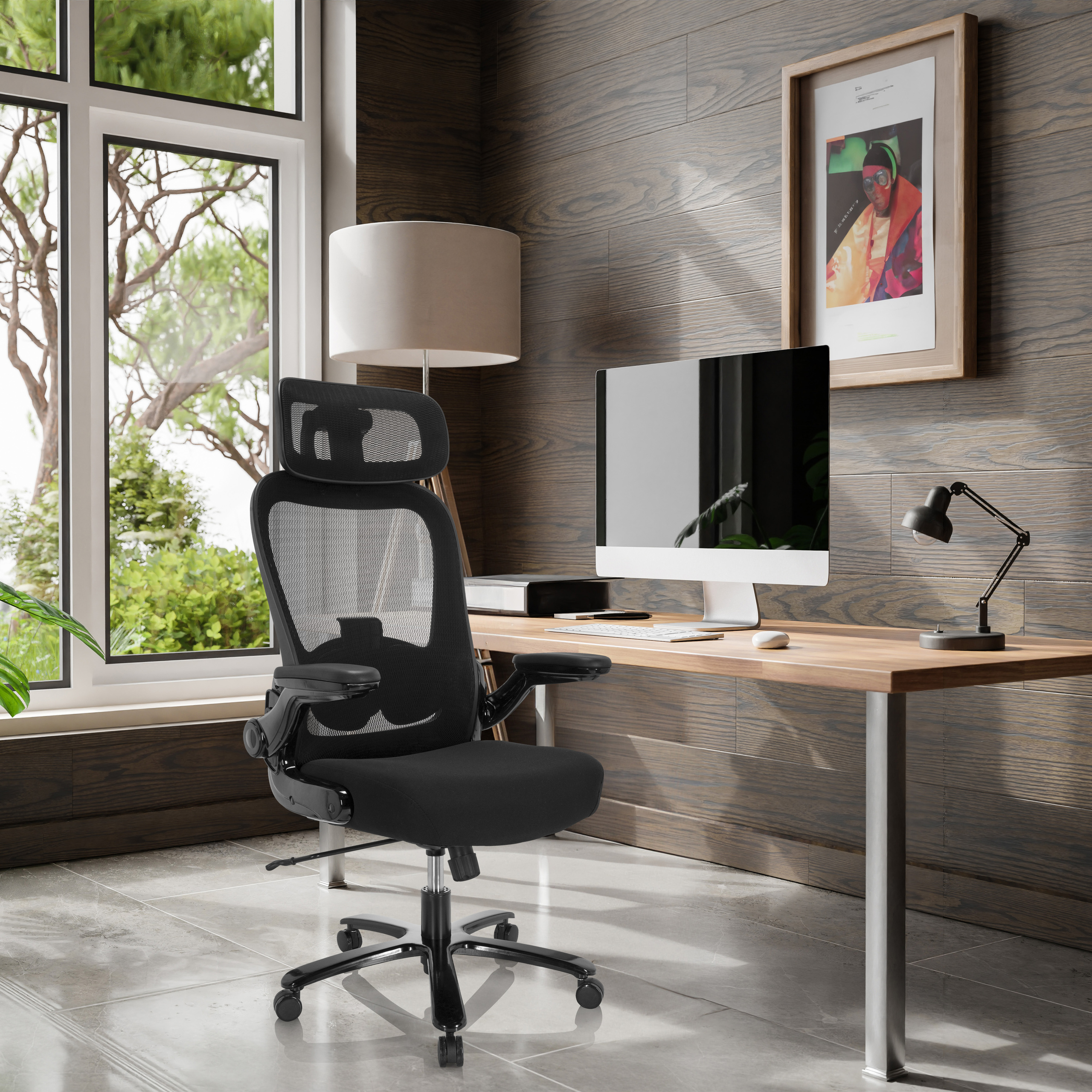 Schwarzer Bürostuhl in einem Homeoffice-Setting. Schreibtisch, Lampe, Fenster und Gemälde sind im Hintergrund.