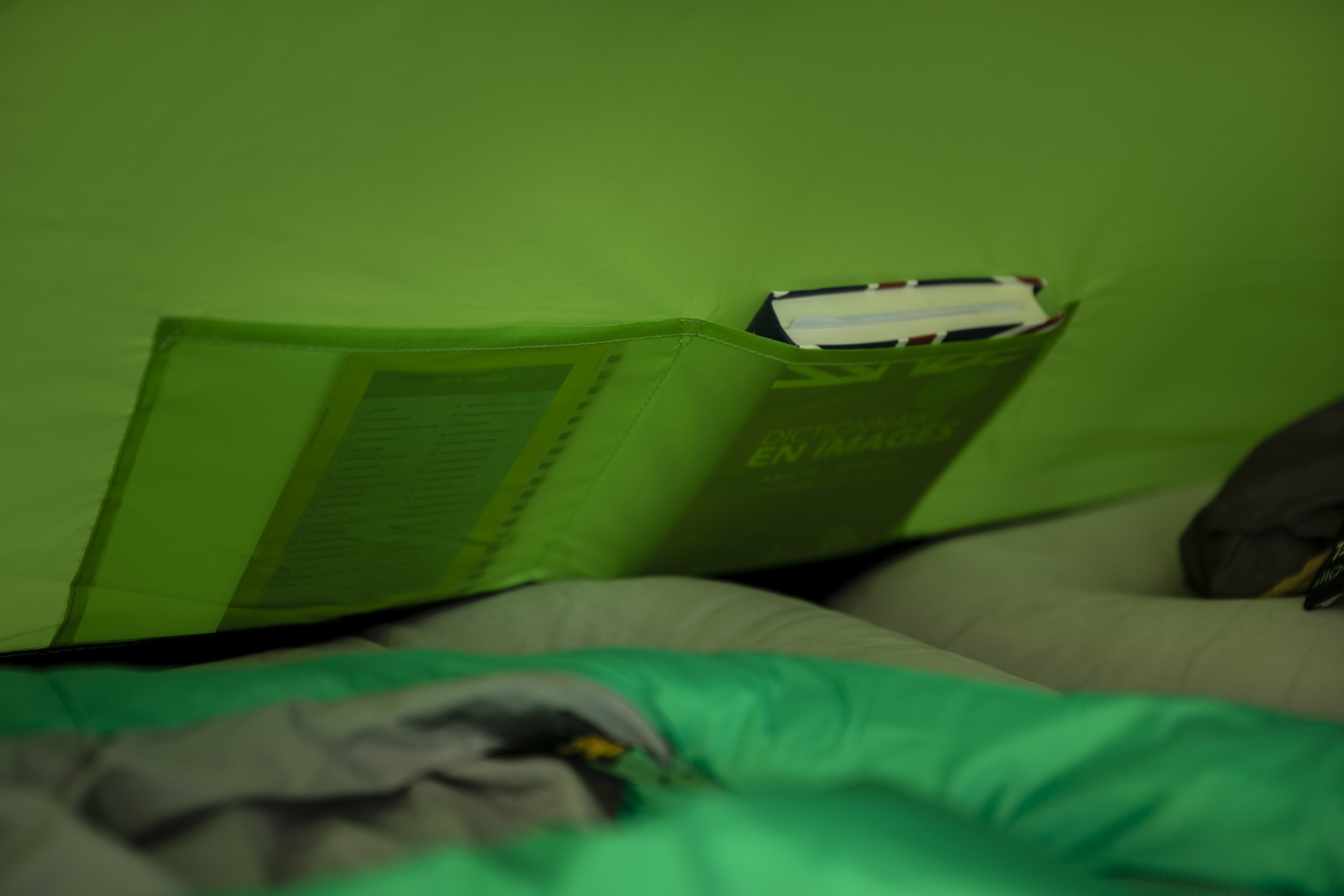 In einem Zelt liegt ein Buch in einer Tasche. Ein grüner Schlafsack liegt am Boden.