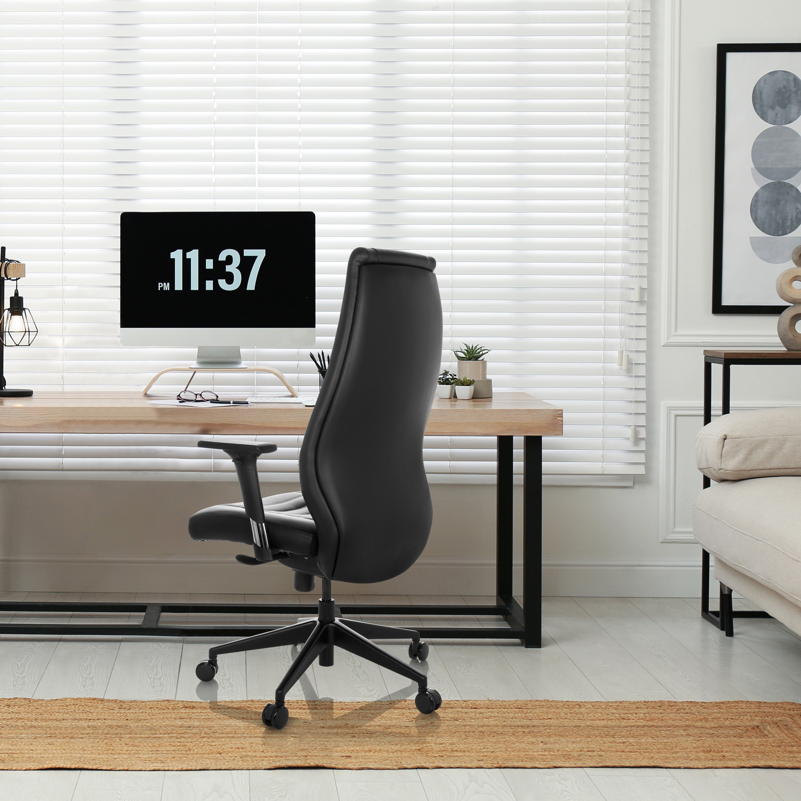 Büro. Schreibtisch, Computerbildschirm, schwarzer Bürostuhl, Fensterjalousien, Teppich, Sofa, Wandkunst.