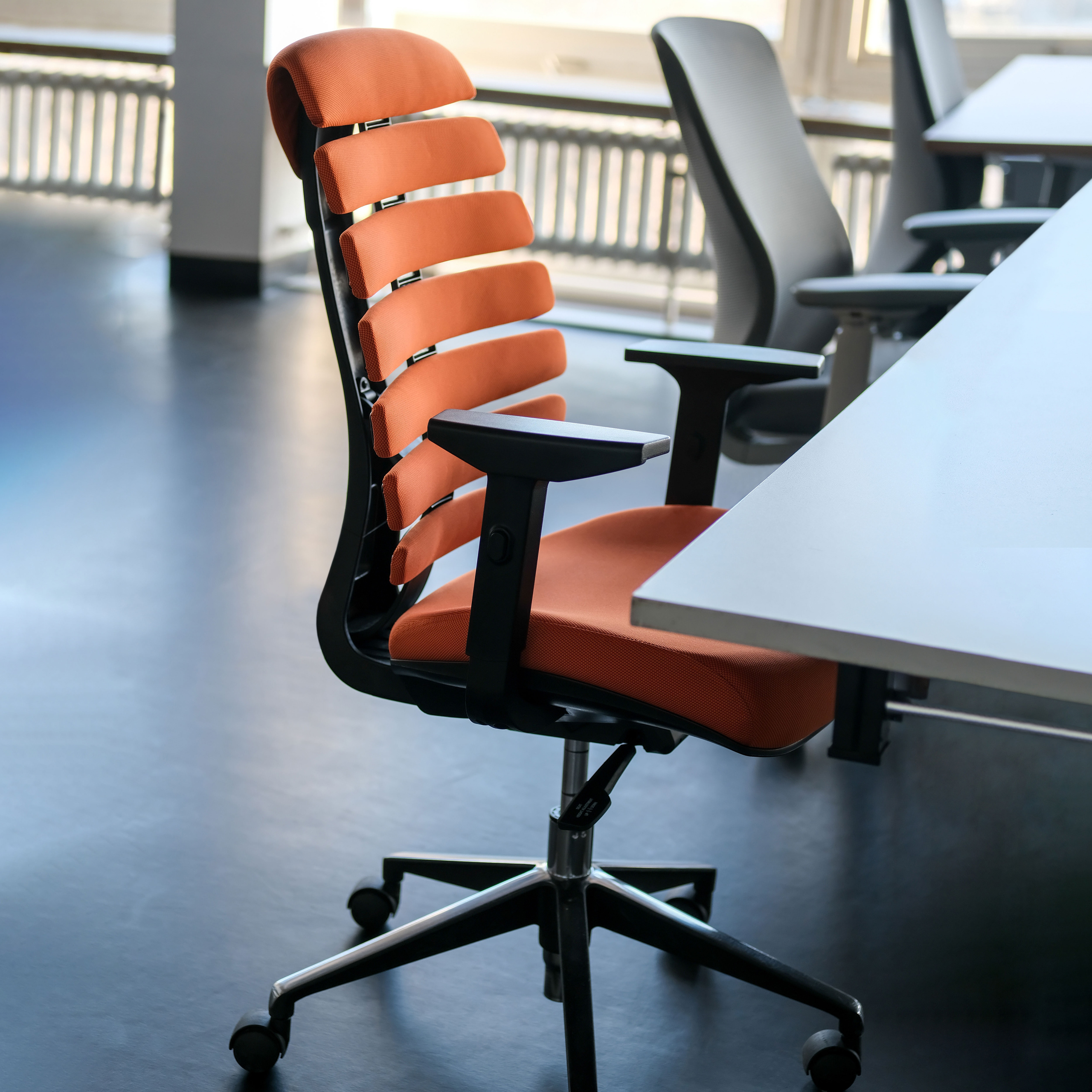 Oranger Bürostuhl mit schwarzem Rahmen, in einem Büro mit Tisch.