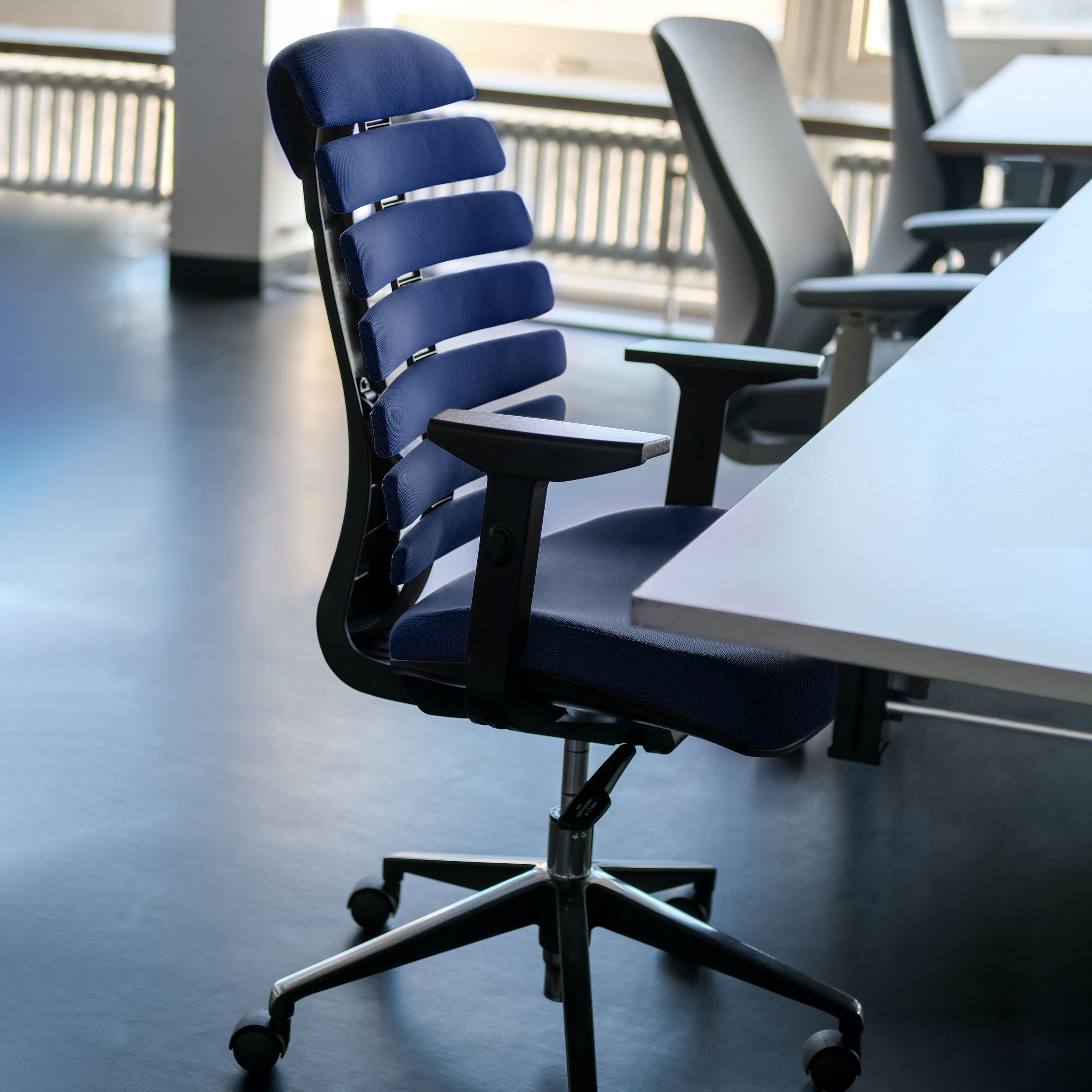 Blauer Bürostuhl mit horizontalen Rückenleisten in einem Büroumfeld.