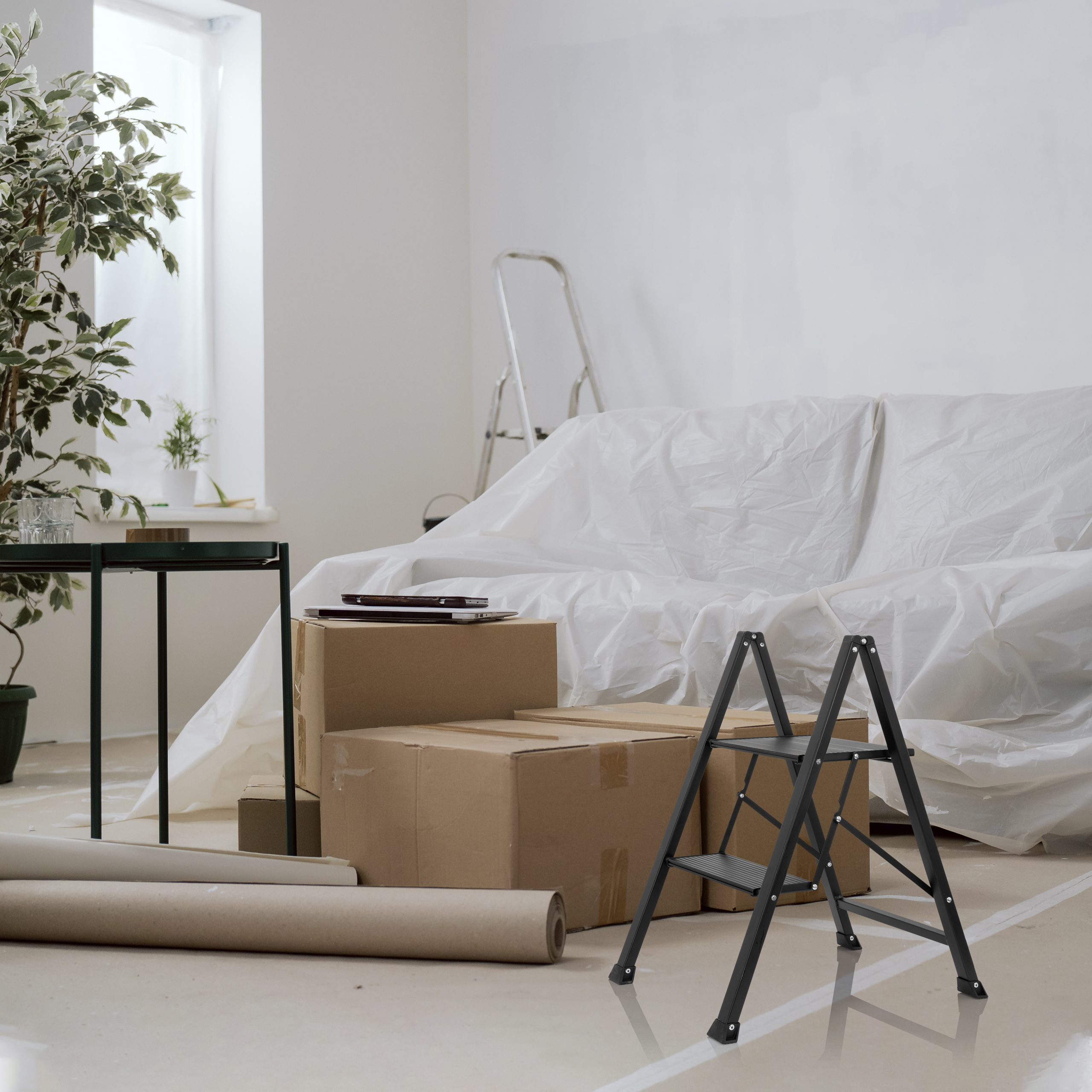 Schwarze Trittleiter, Kartons und ein weiß bedecktes Sofa in einem Raum mit Fenster.