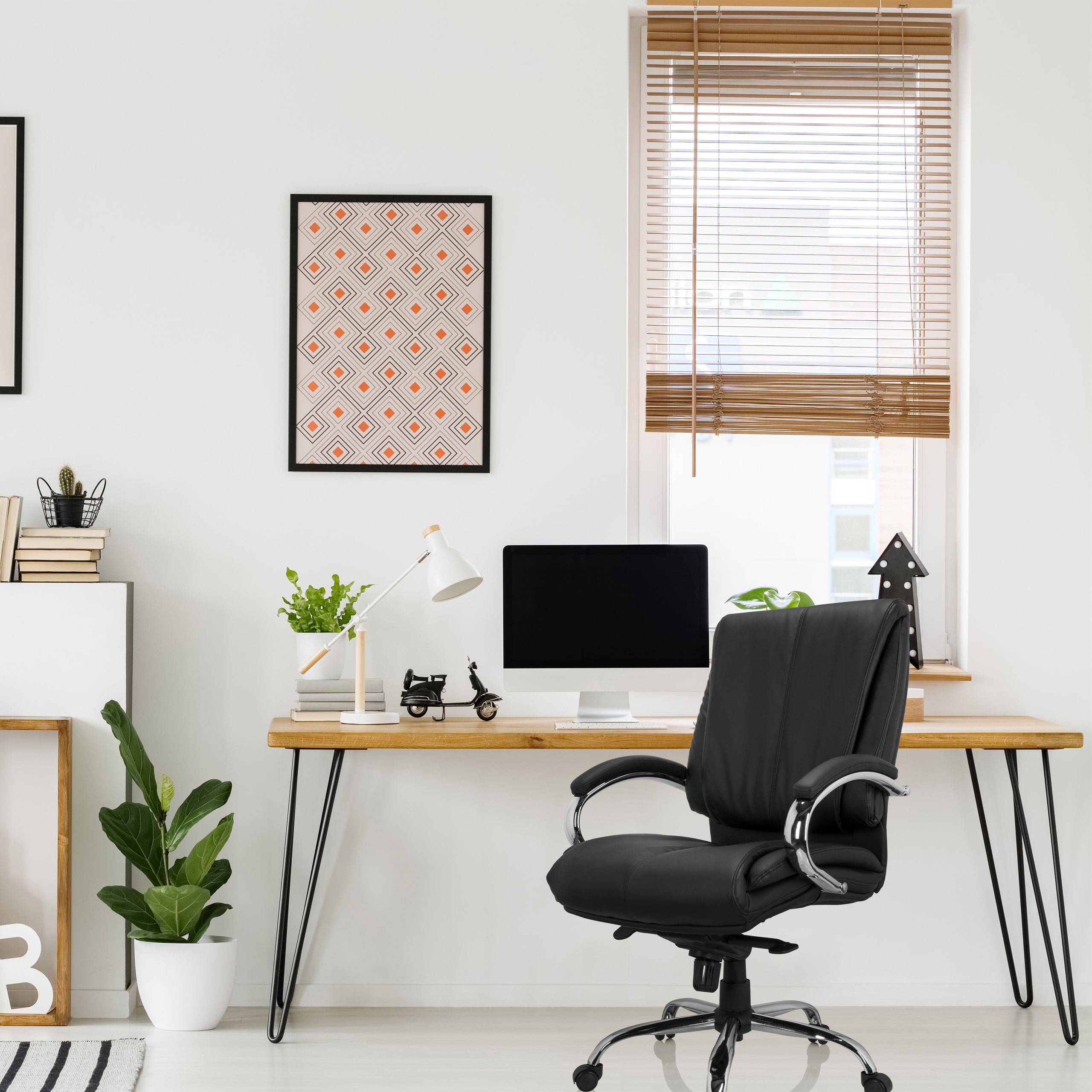 Büro mit schwarzem Stuhl, Holzschreibtisch, Computer, gerahmter Kunst und Fenster.