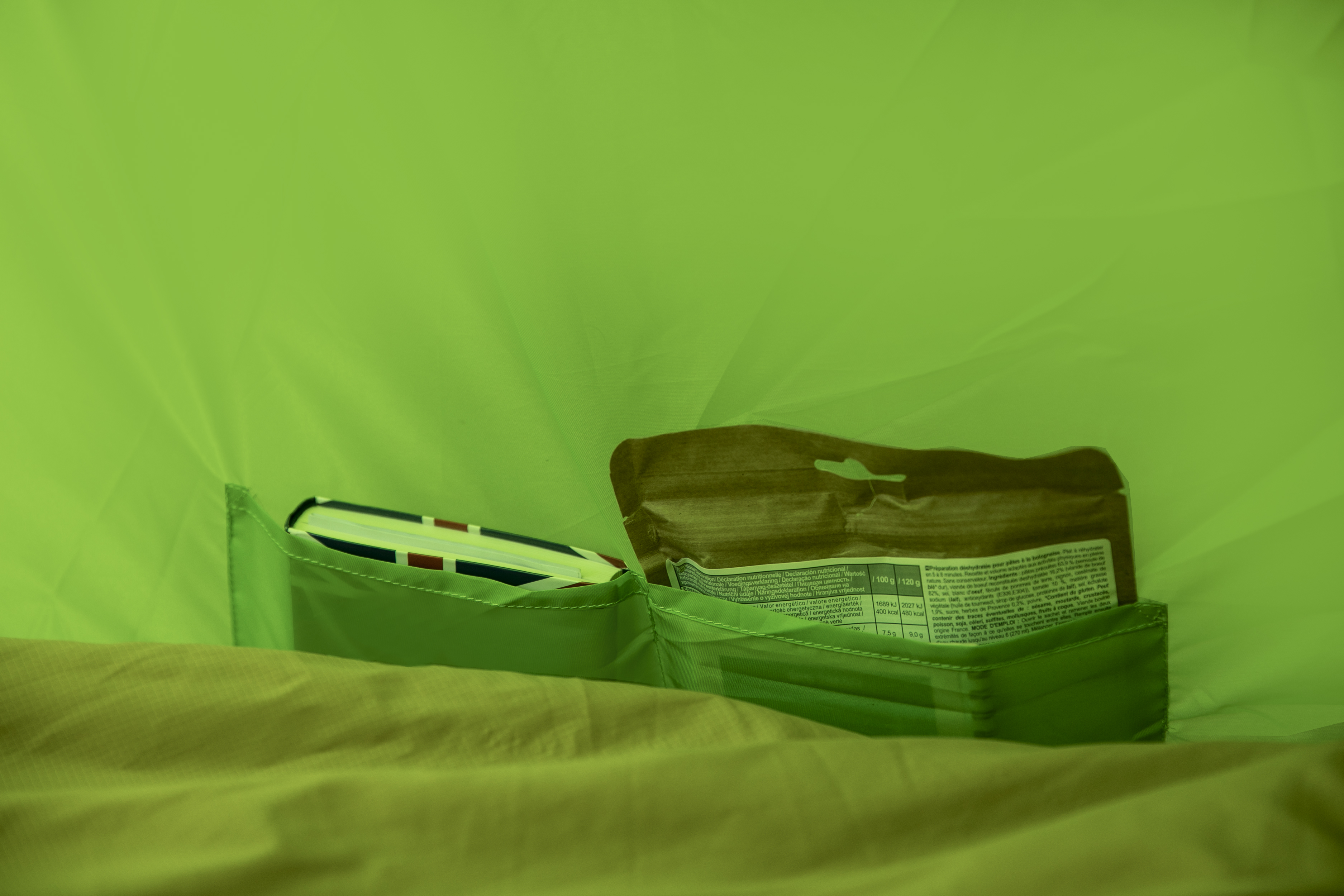In einem grünen Zelt. Notizbuch, Stift und Lebensmittelpaket in einer grünen Tasche.