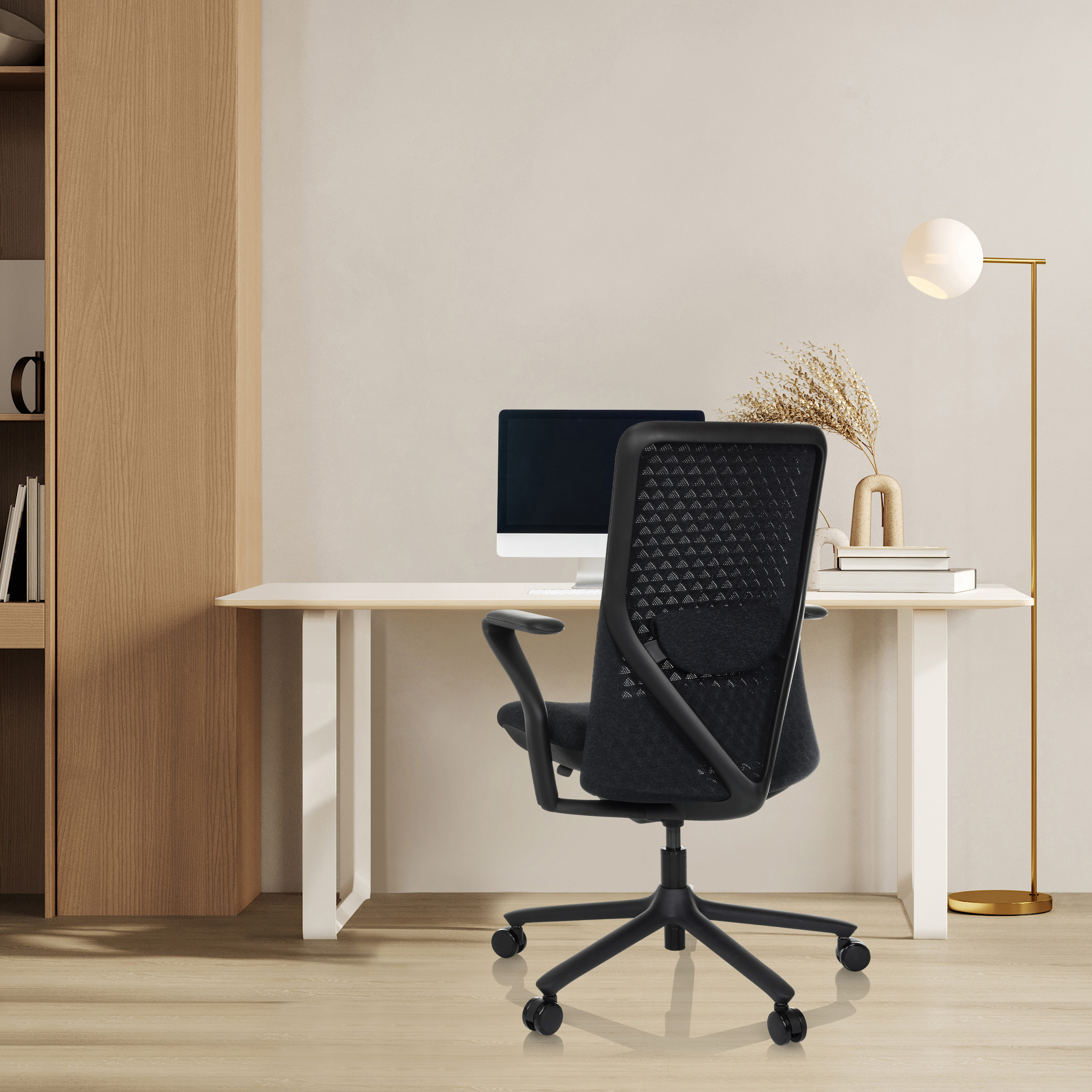 Schreibtisch mit schwarzem Stuhl, Computer und Lampe. Holzschrank links.