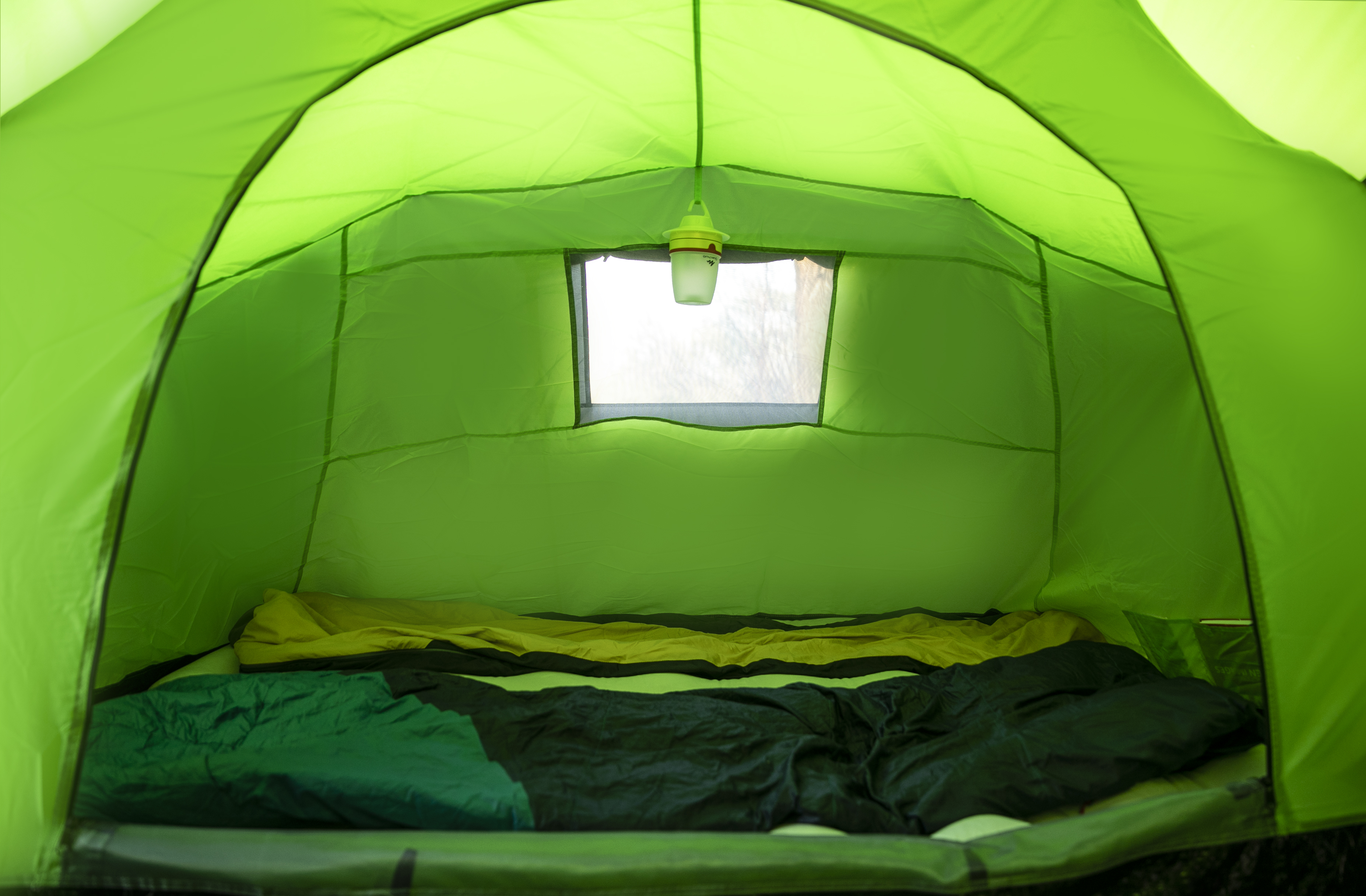 In einem grünen Zelt. Schlafsack und Kissen sind sichtbar. Eine Lampe hängt von oben.