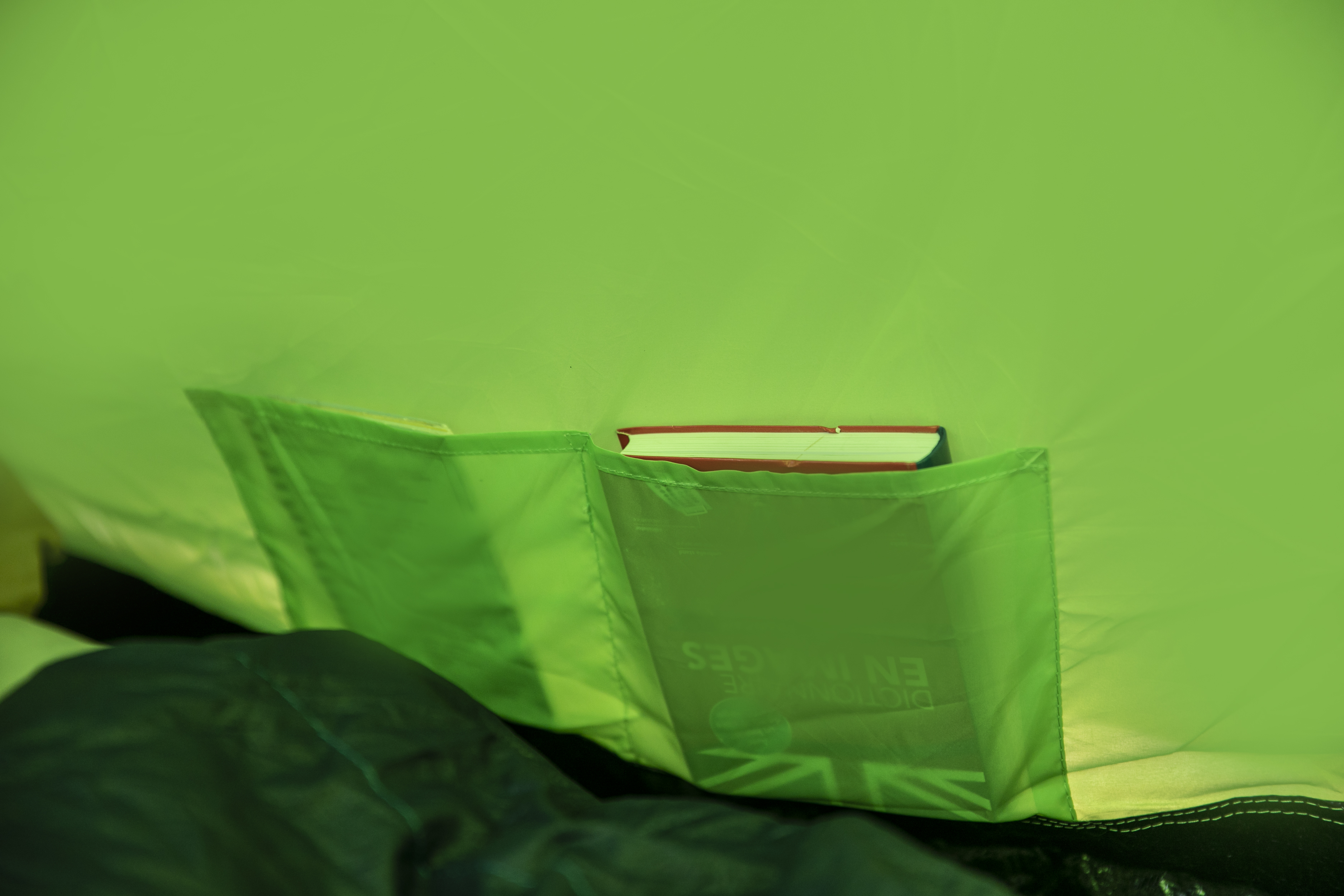 In einem grünen Zelt hält eine Tasche ein Buch und einen Notizblock.