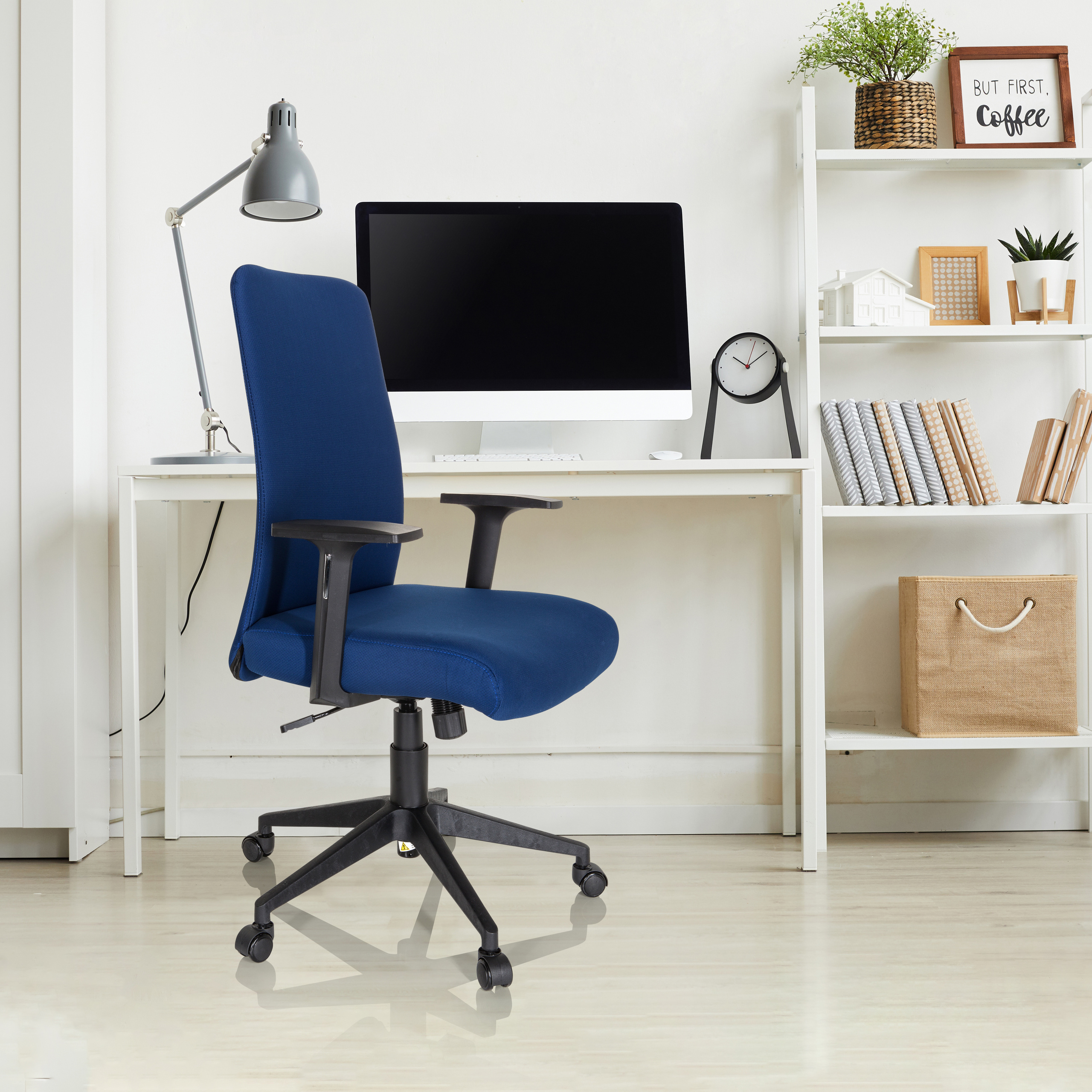 Büro mit blauem Stuhl, Schreibtisch, Computer und Regalen mit Gegenständen. Weiße Wände und Boden.