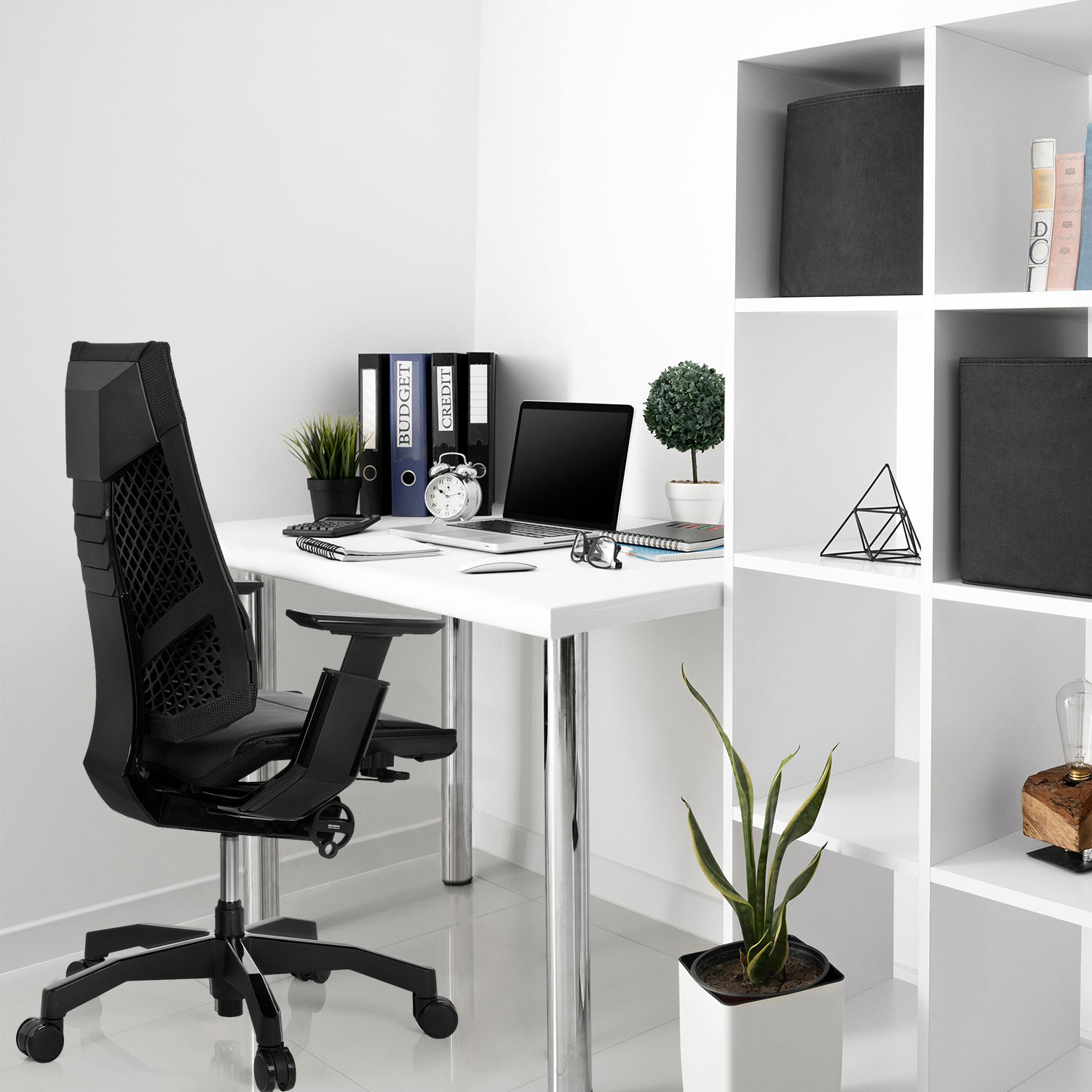 Büro-Setup: schwarzer Stuhl, weißer Schreibtisch mit Laptop, weiße Regale mit Gegenständen und Pflanzen.