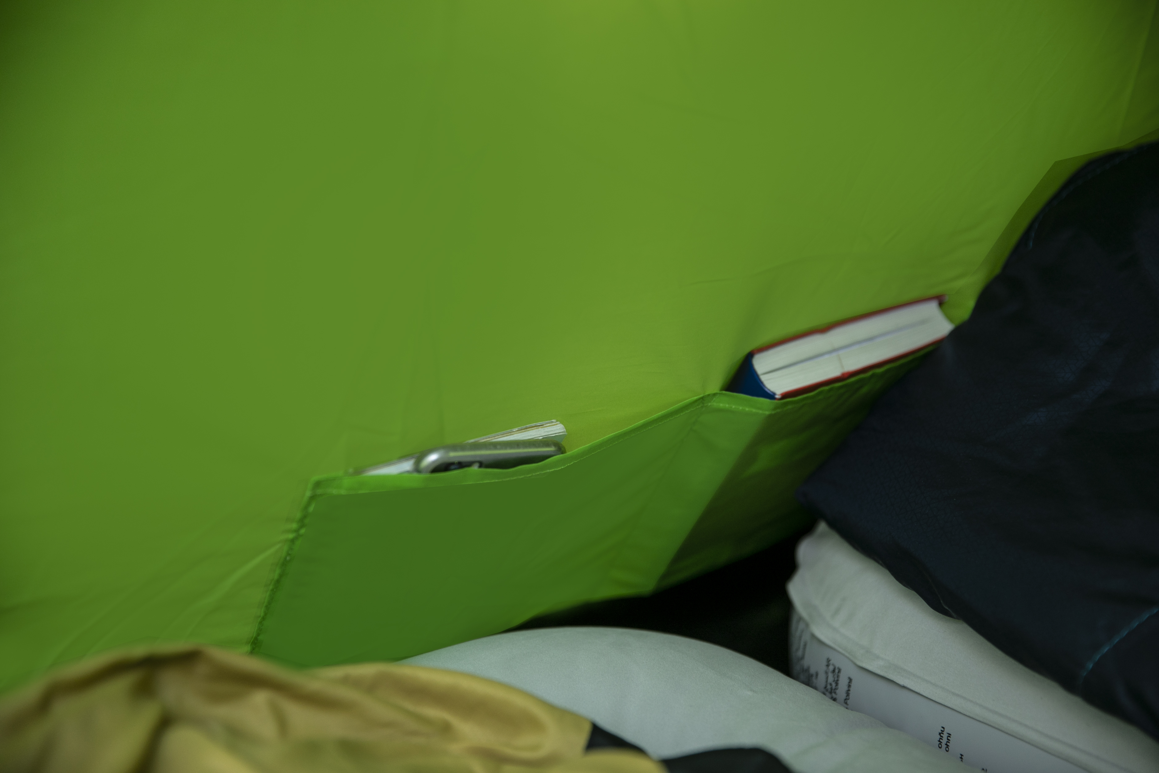 Dentro de una tienda verde, un bolsillo contiene un teléfono y un libro. El interior de la tienda es visible.