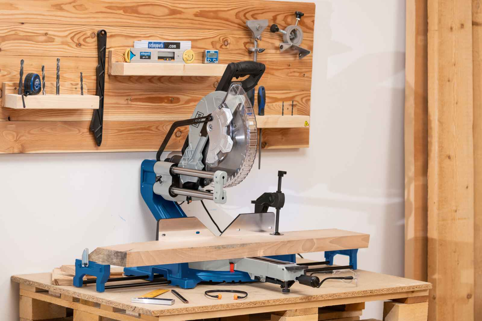Een verstekzaag op een houten pallettafel, met een houten plank die wordt gezaagd. Een pegboard op de achtergrond.