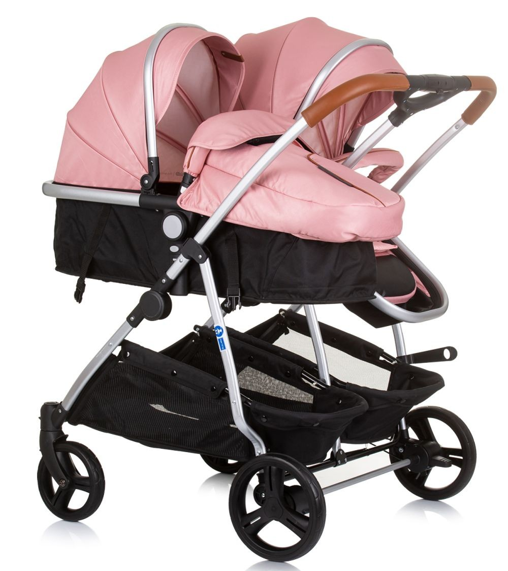 Rosa Doppelkinderwagen mit zwei Sitzen. Der Kinderwagen hat ein silbernes Gestell, rosa Verdecke und schwarze Körbe.