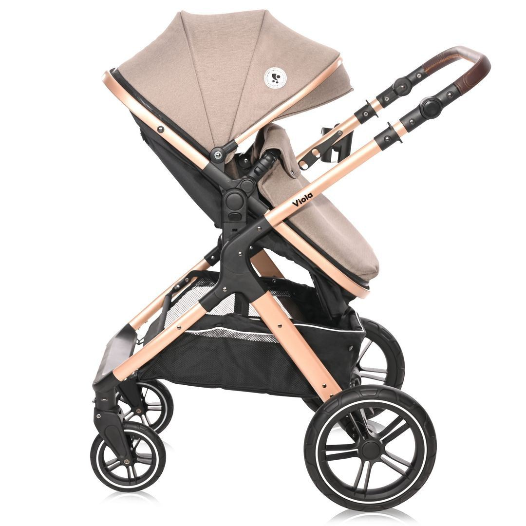 Cochecito beige y negro, visto de lado. Tiene un asa marrón y un marco oro rosa.