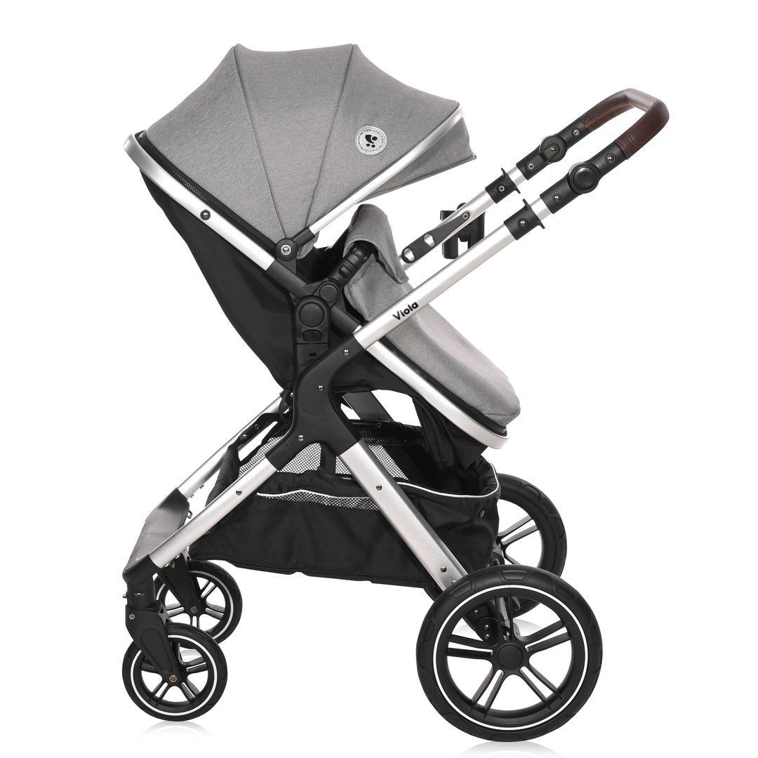 Grauer Kinderwagen mit silbernem Rahmen, schwarzem Korb und braunem Griff. Seitenansicht.