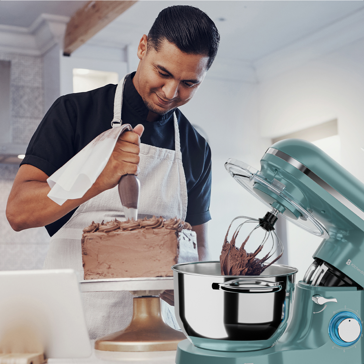 Man versiert een chocoladetaart met glazuur, met een mixer op de achtergrond.