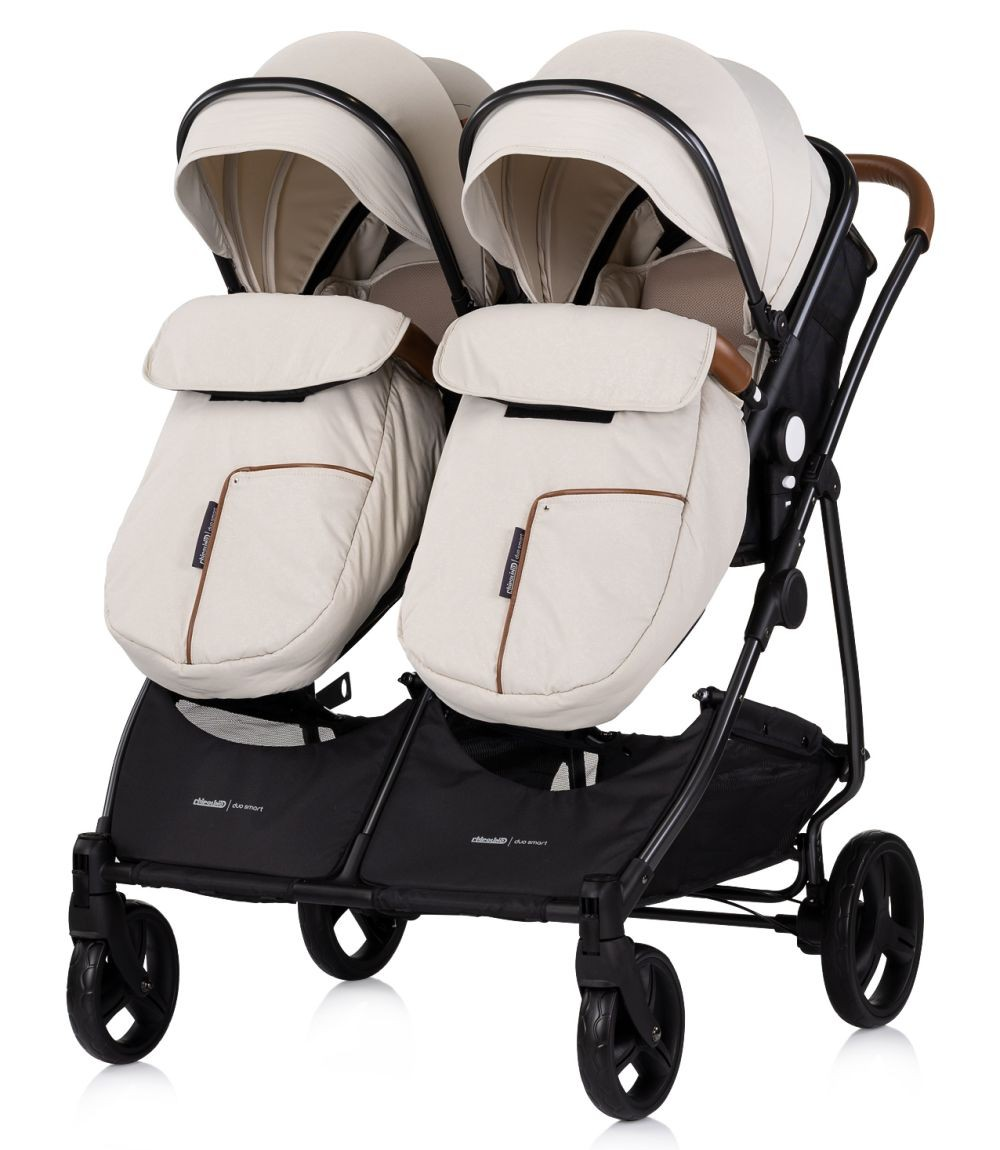 Beiger Doppelkinderwagen mit schwarzen Akzenten und Bezügen auf weißem Hintergrund.